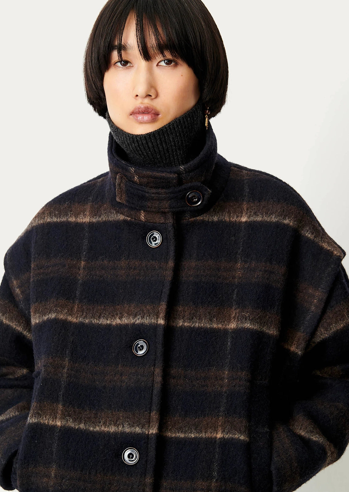 A woman wearing a navy blue and brown plaid short jacket with funnel neck and button front.