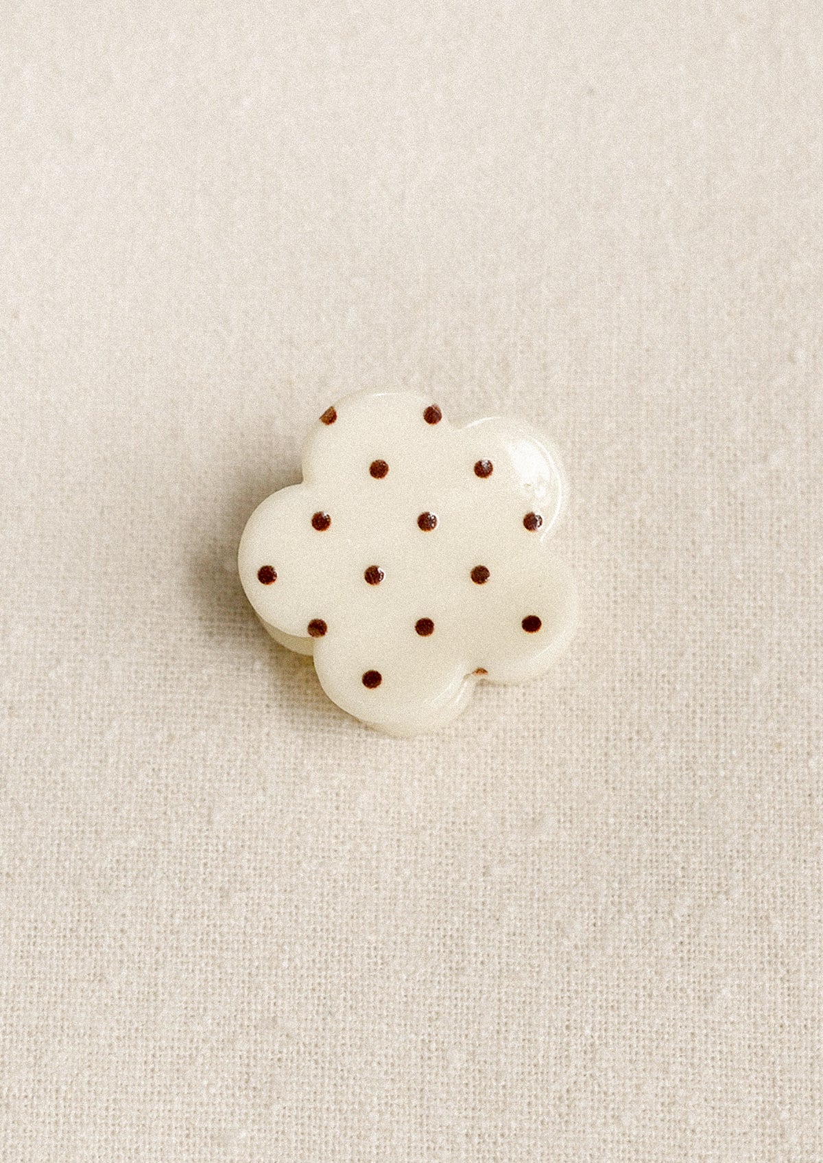 A small flower shaped hair clip in cream with burgundy polka dots.