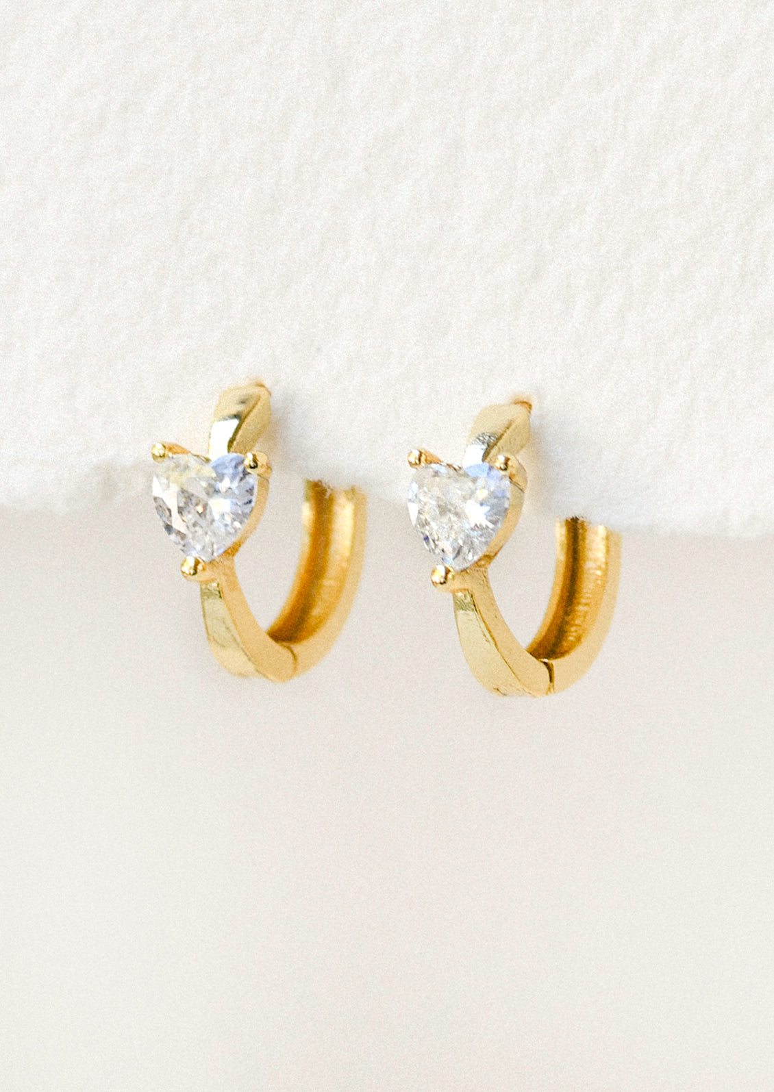 A pair of gold hoop earrings with heart shaped cubic zirconia gems.