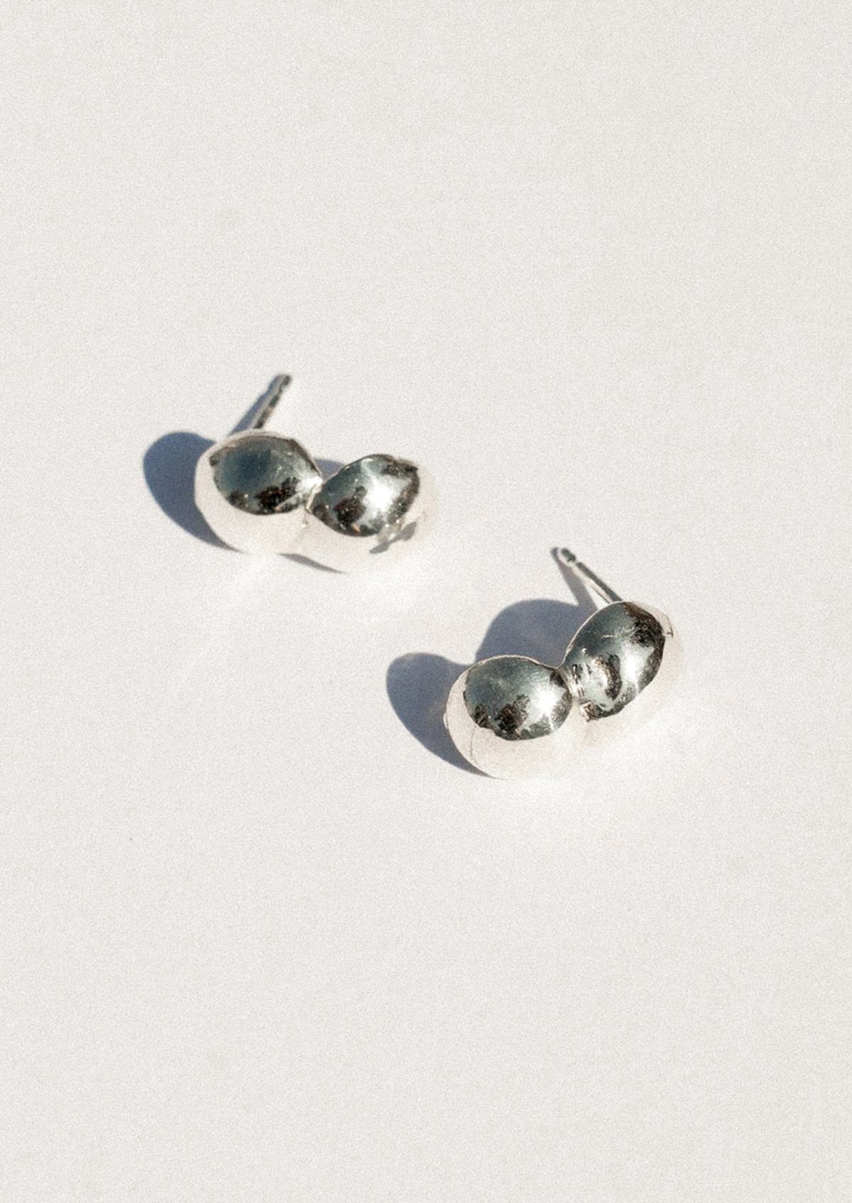 A pair of silver stud earrings with a unique double-oval design, photographed on a clean white background with soft shadows.