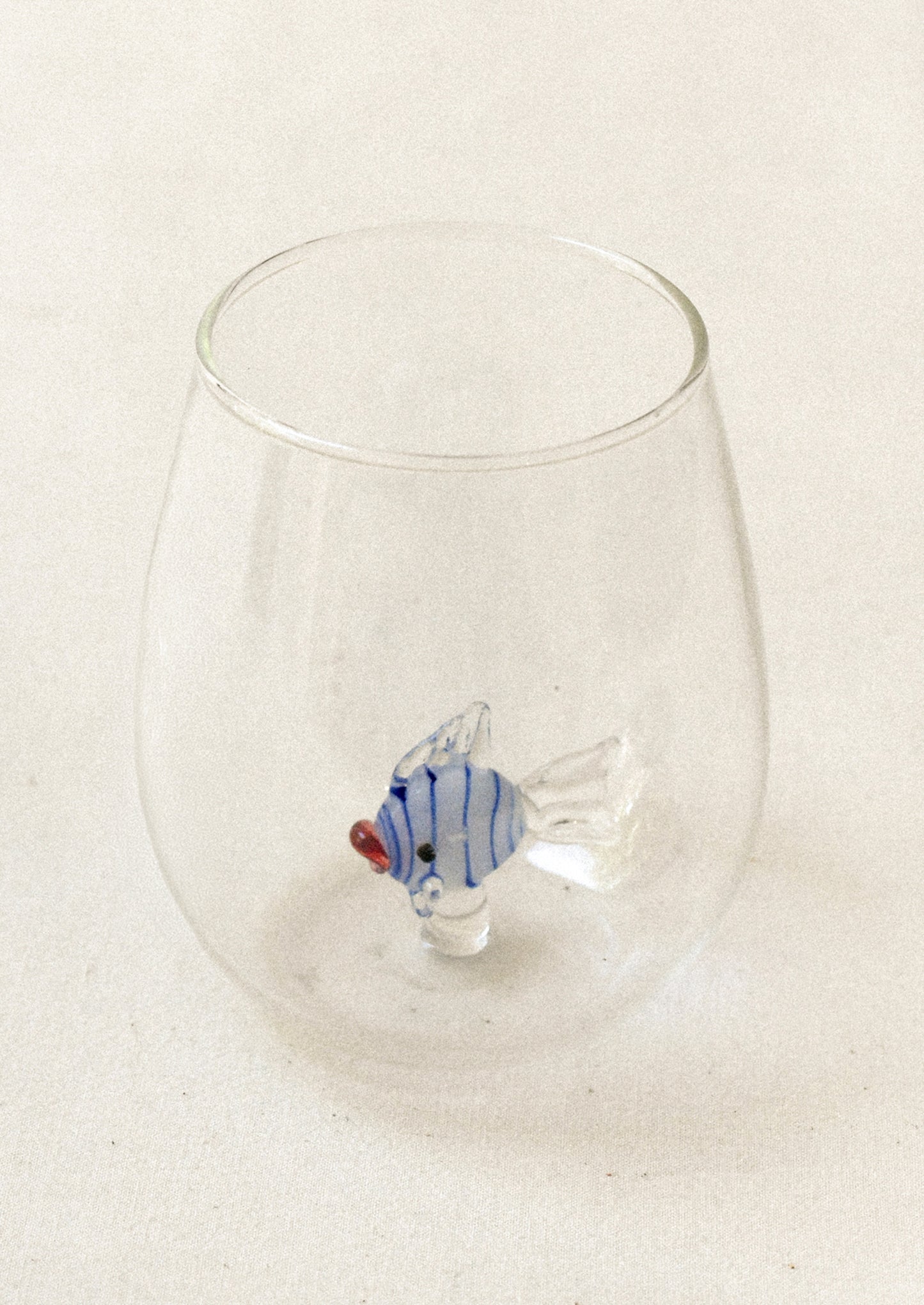 A clear tumbler glass with lampwork fish detail at inner bottom.