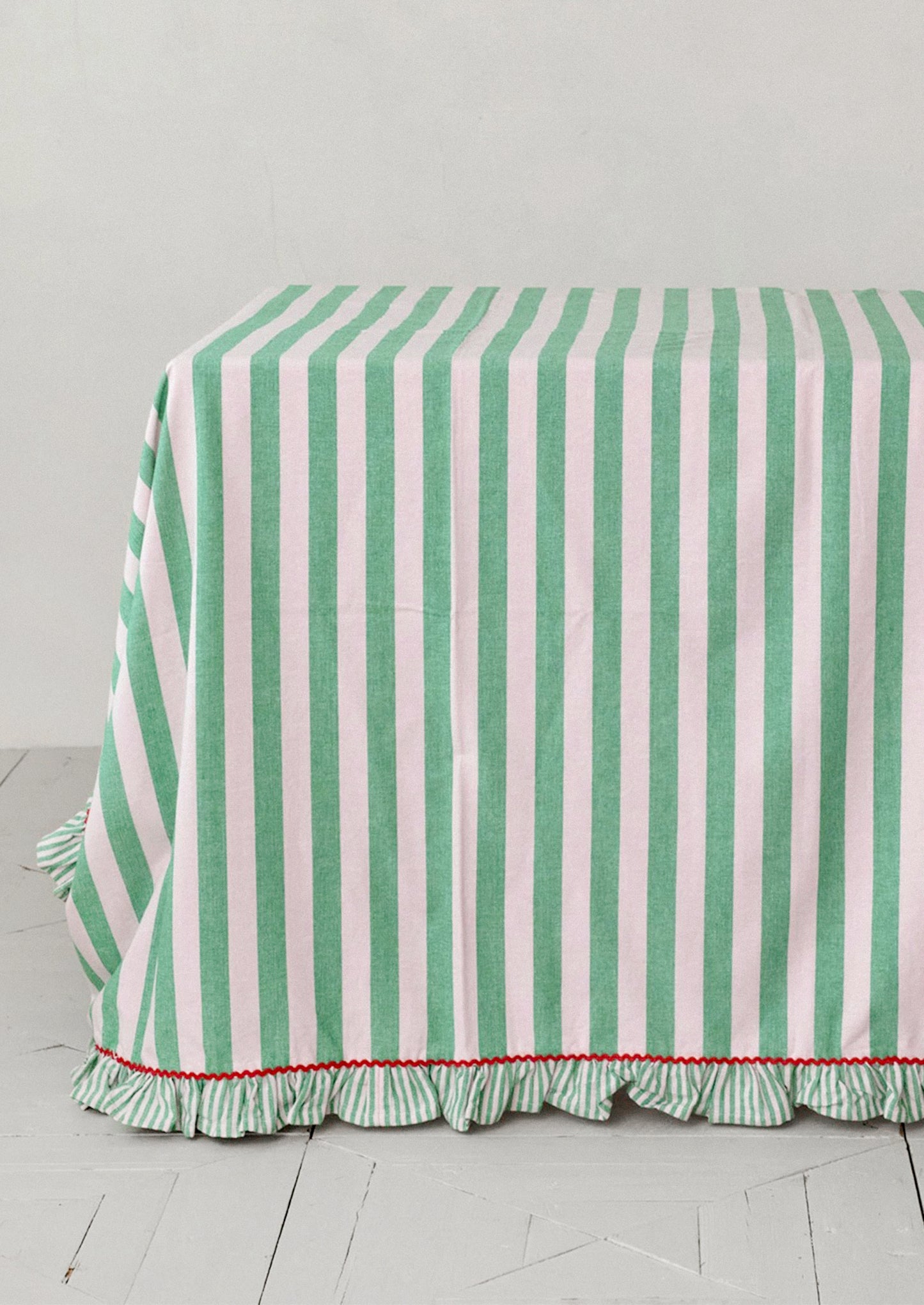 A tablecloth with wide blush and green stripes and red ricrac ruffle trim.