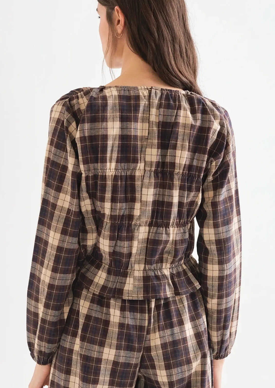 A woman wearing a long sleeve plaid top in brown, blue and cream with smocked detailing throughout.