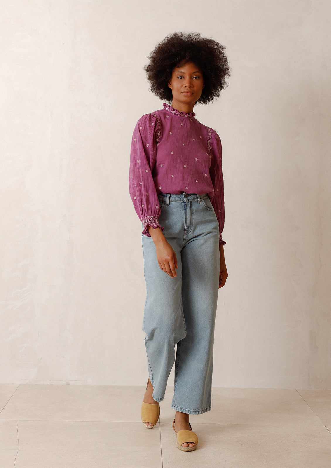 Woman wearing magenta top with embroidered details, blue jeans, and flats.
