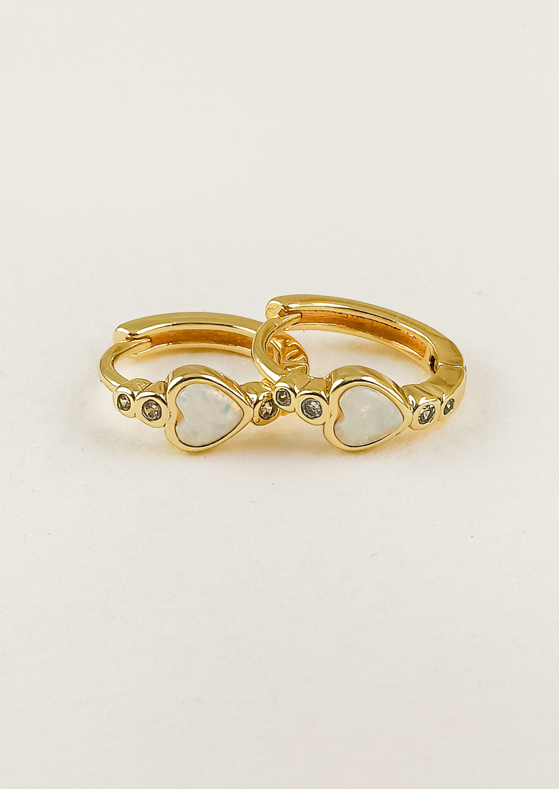 A pair of gold hoop earrings with a heart=shaped opal in the center and tiny gems above and below.