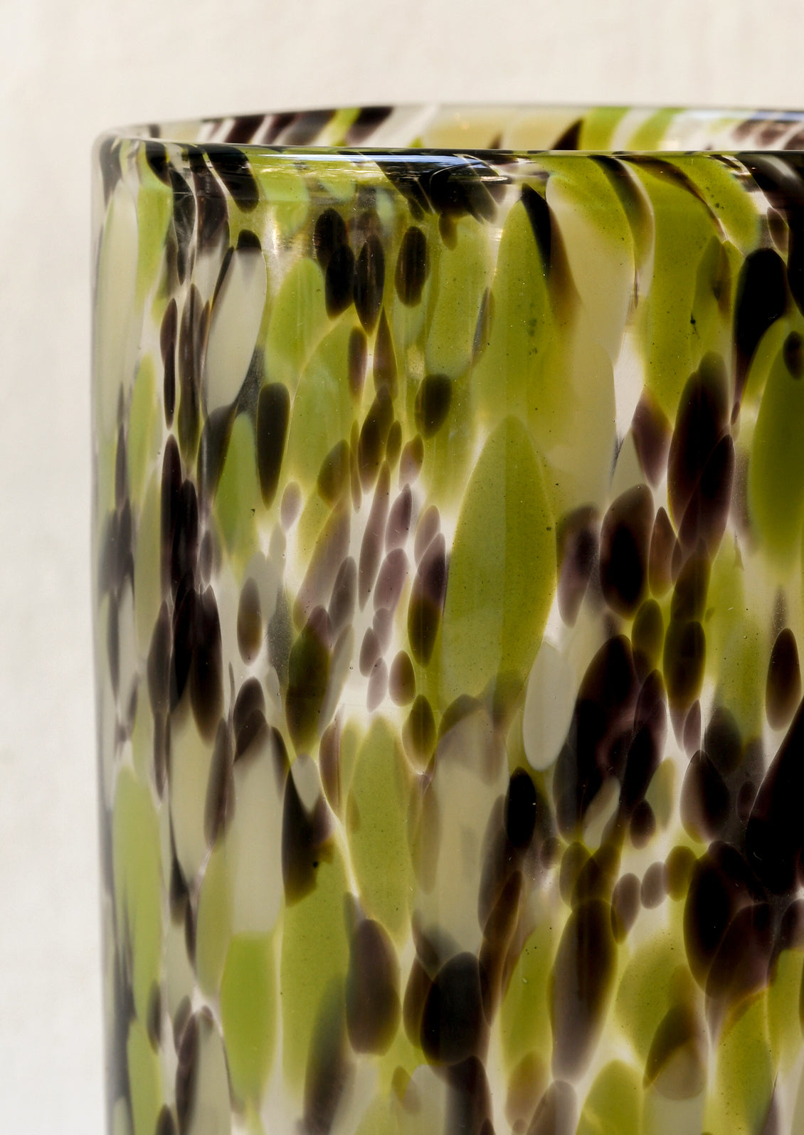 Closeup of a tall cylindrical glass vase with a green and brown painted design.