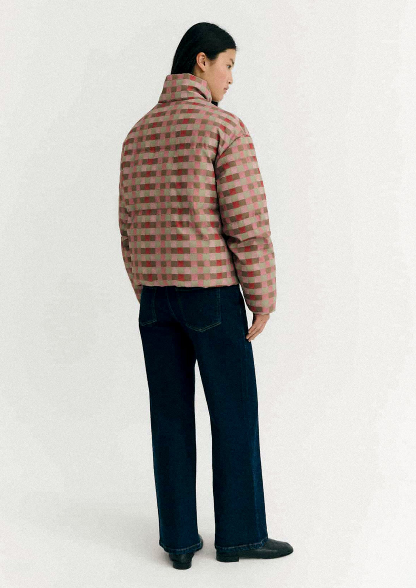 Person wearing a checkered puffer jacket on a white background.