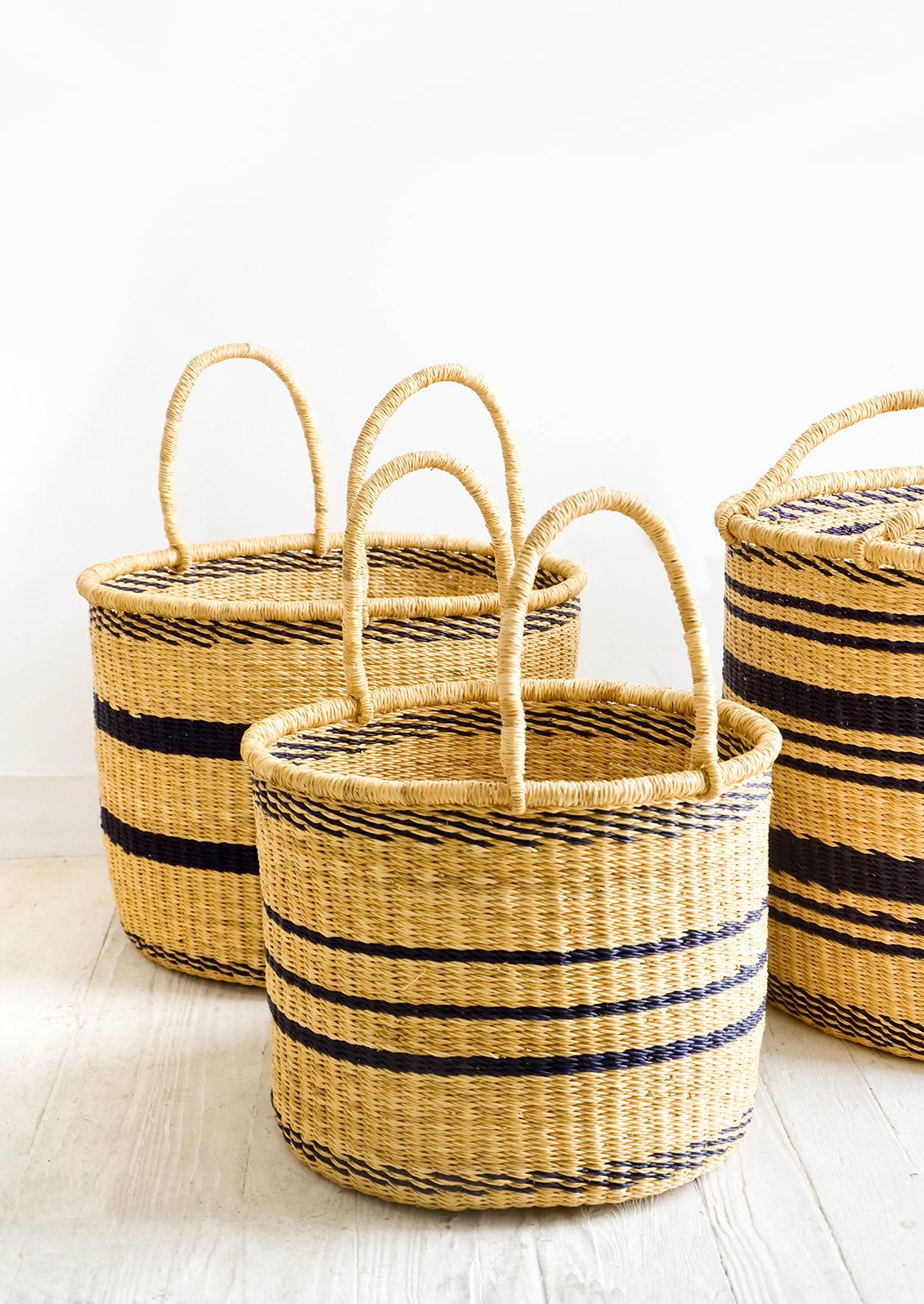 Group of round straw storage baskets with handles at top and navy blue stripes throughout
