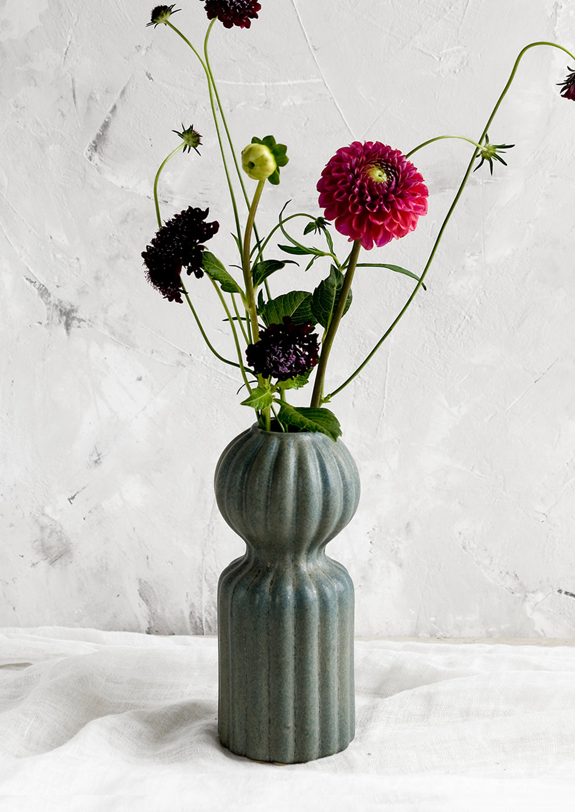 A curvy ceramic vase in teal glaze with ball-shaped top, holding flowers.