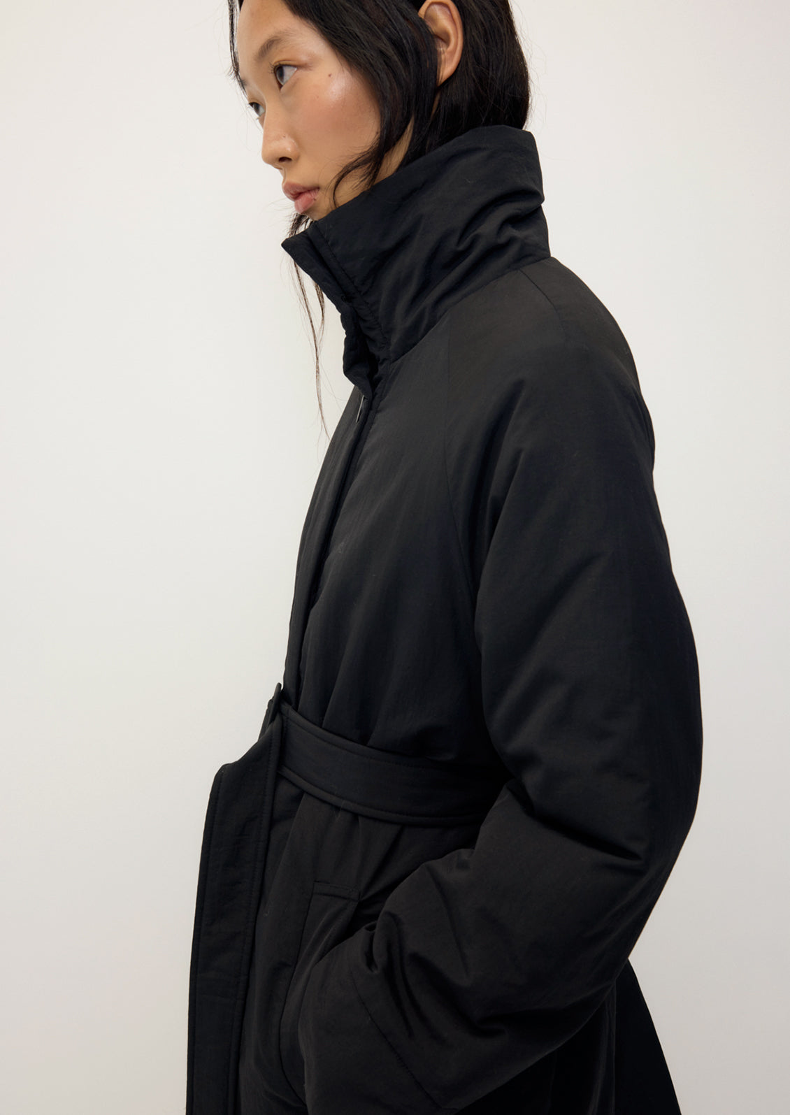 A person wearing a long black winter coat with matching belt.