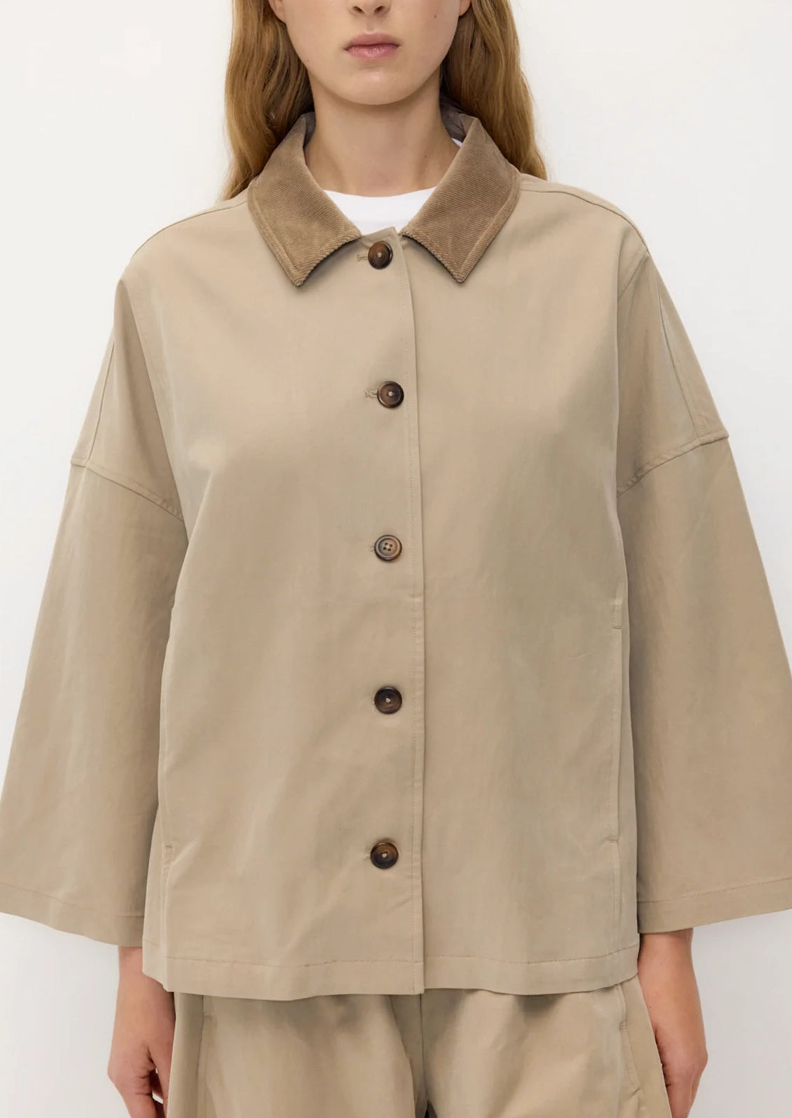 A person wearing a hip-length A-line jacket in khaki with tan contrast collar.