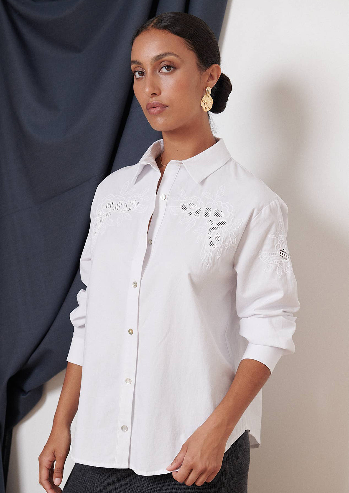A woman wearing a white button down shirt with eyelet embroidery at yoke.