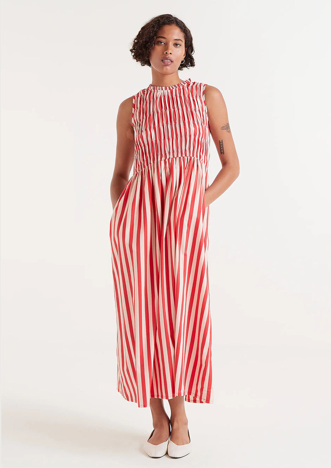 A woman wearing a cotton dress with smocked bodice in vertical red stripes.