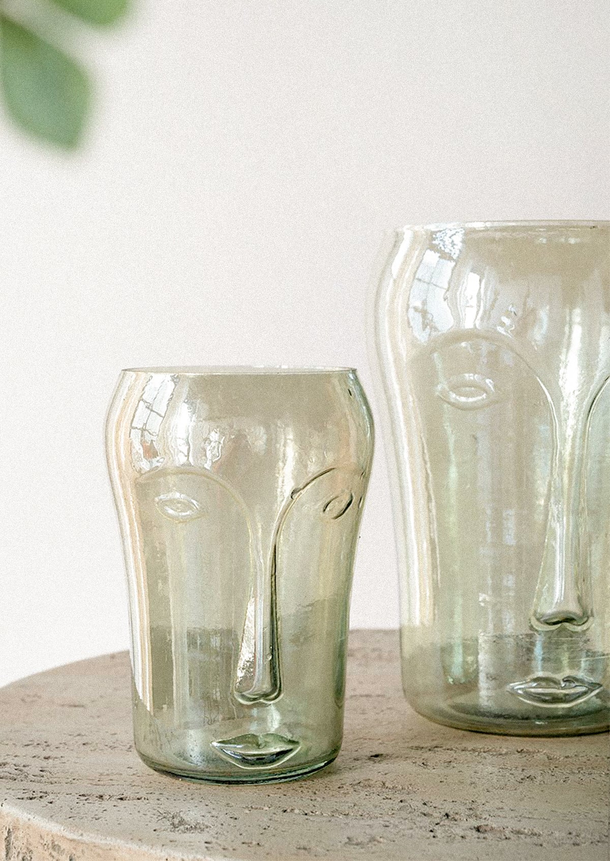 Two translucent smoky green glass vessels with embossed face details.