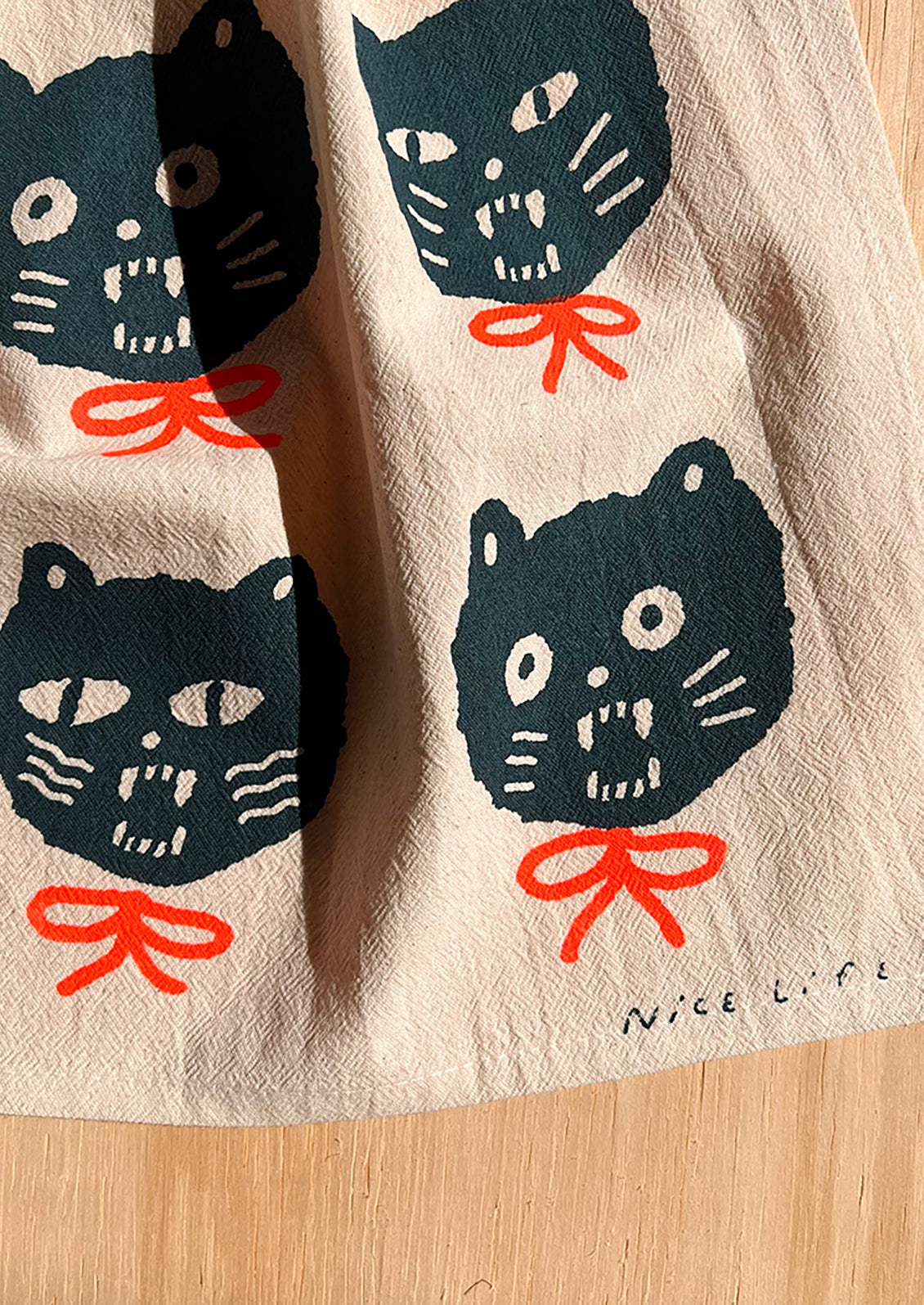 A tea towel with repeating cat face motif.