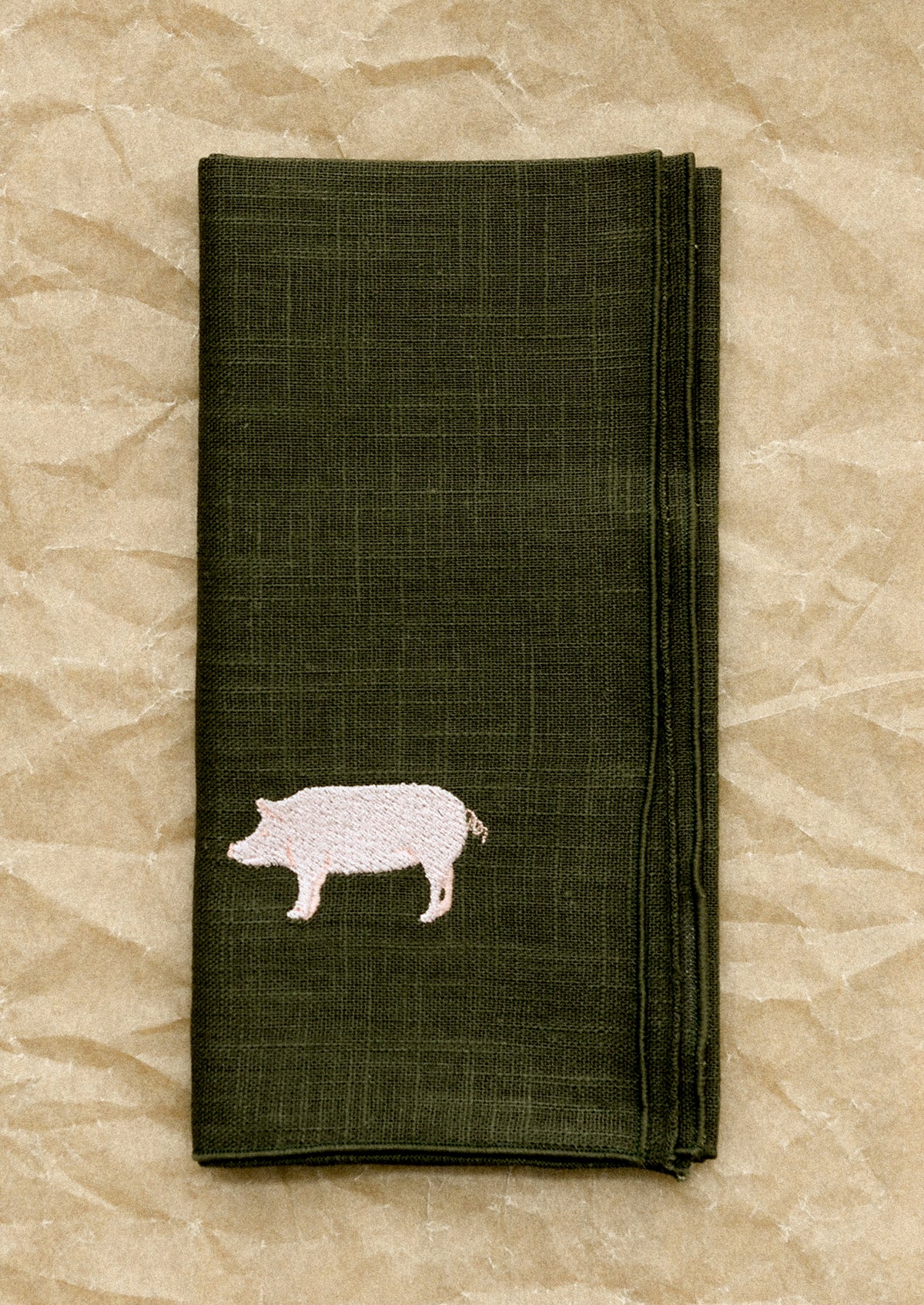 Folded dark green napkin with a pig design on a beige textured background