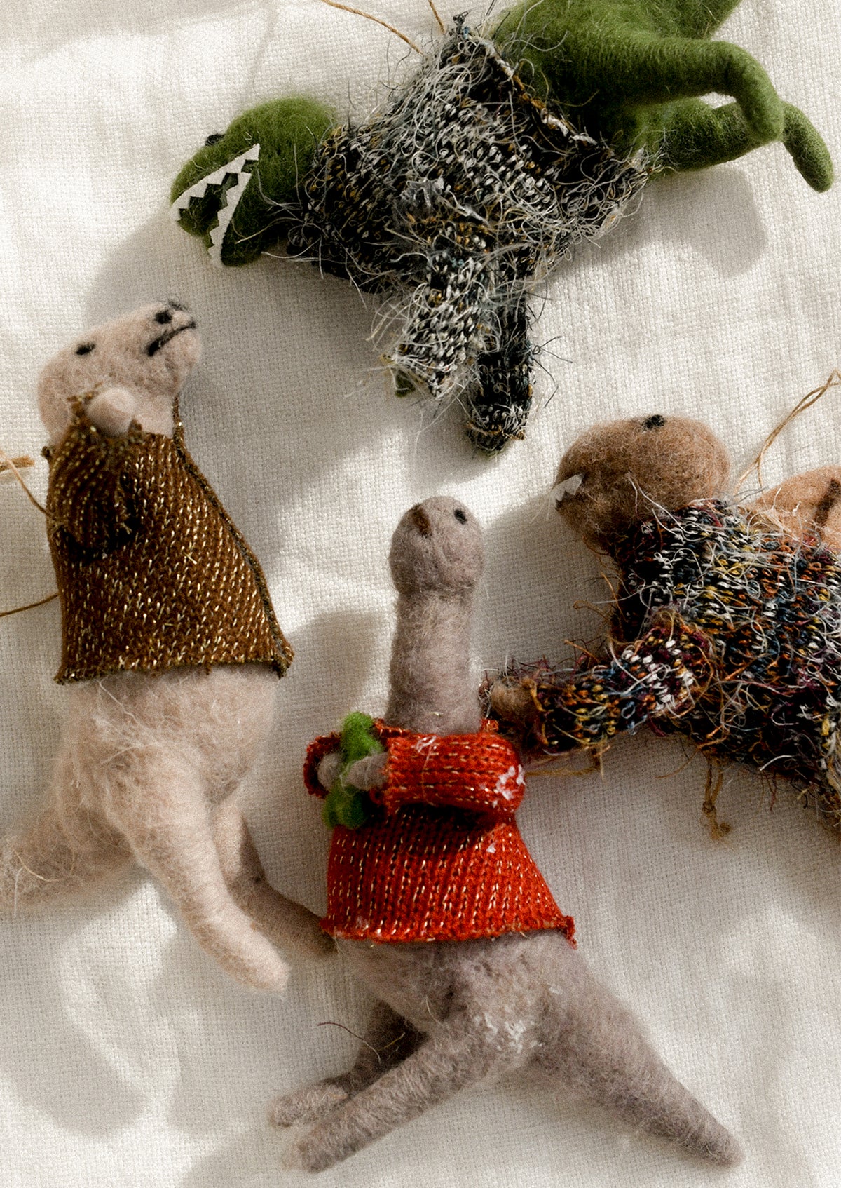 Assorted wool felt ornaments depicting dinosaurs wearing sweaters.