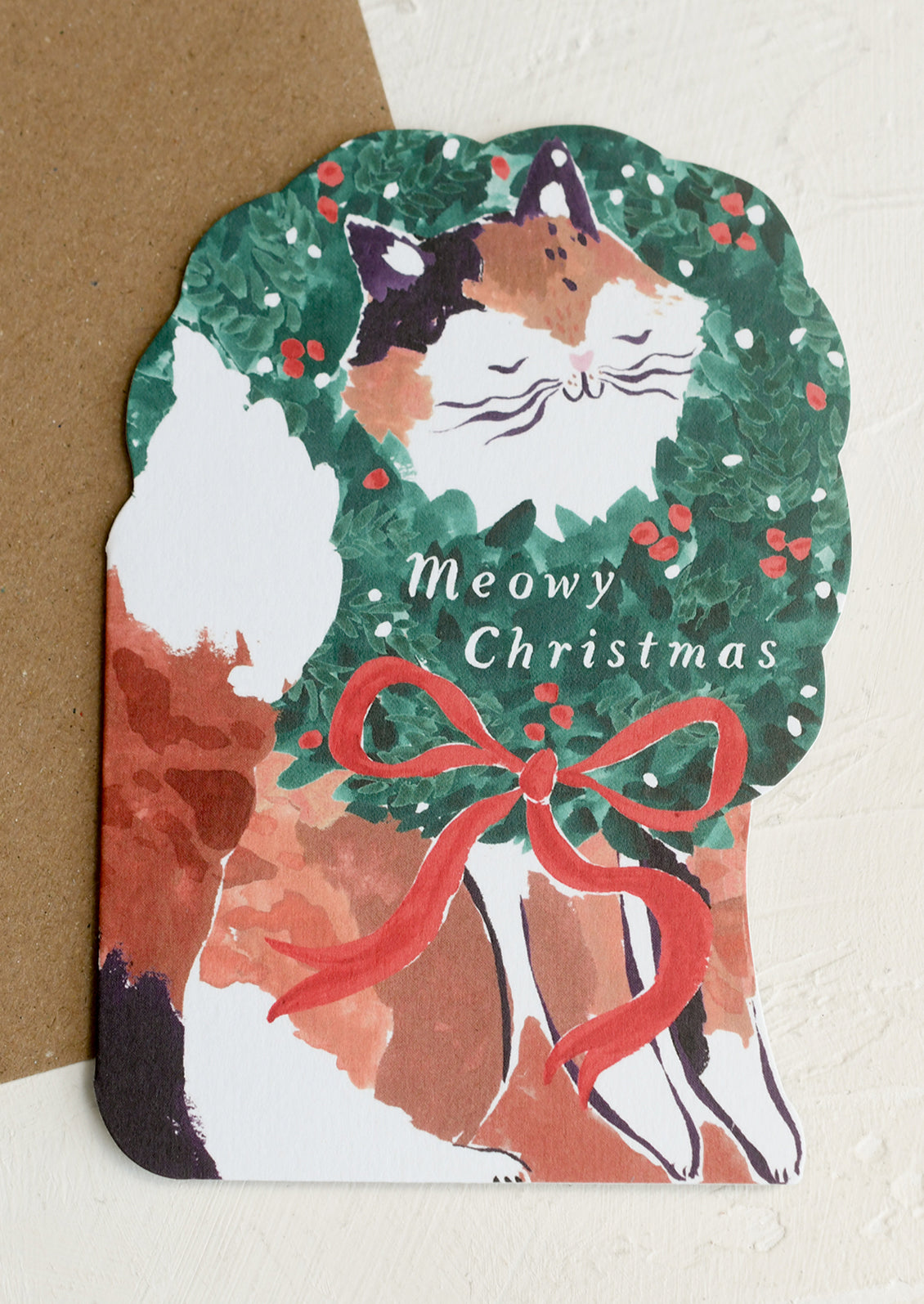 A diecut card depicting a cat wearing a wreath around its neck, text reads "Meowy Christmas".