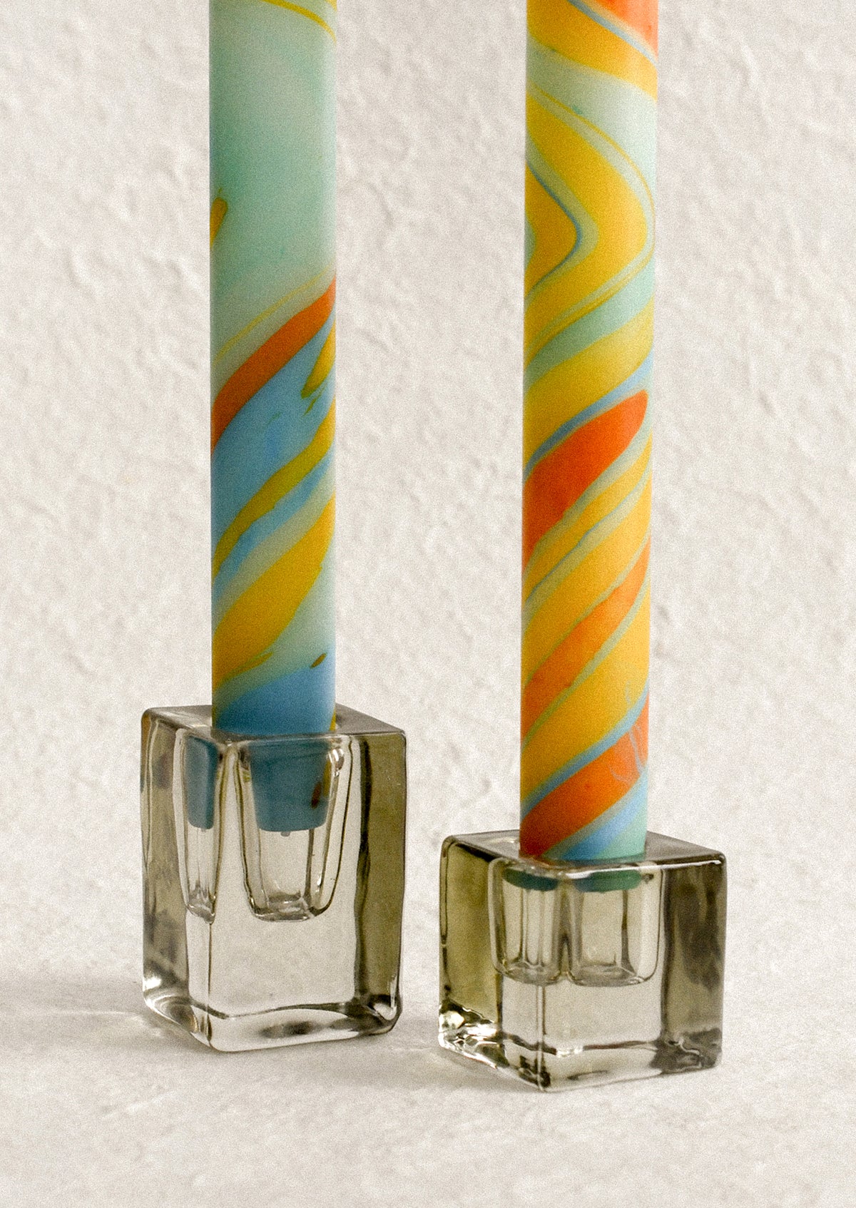 A marbled taper candle in blue, orange and yellow swirl pattern.