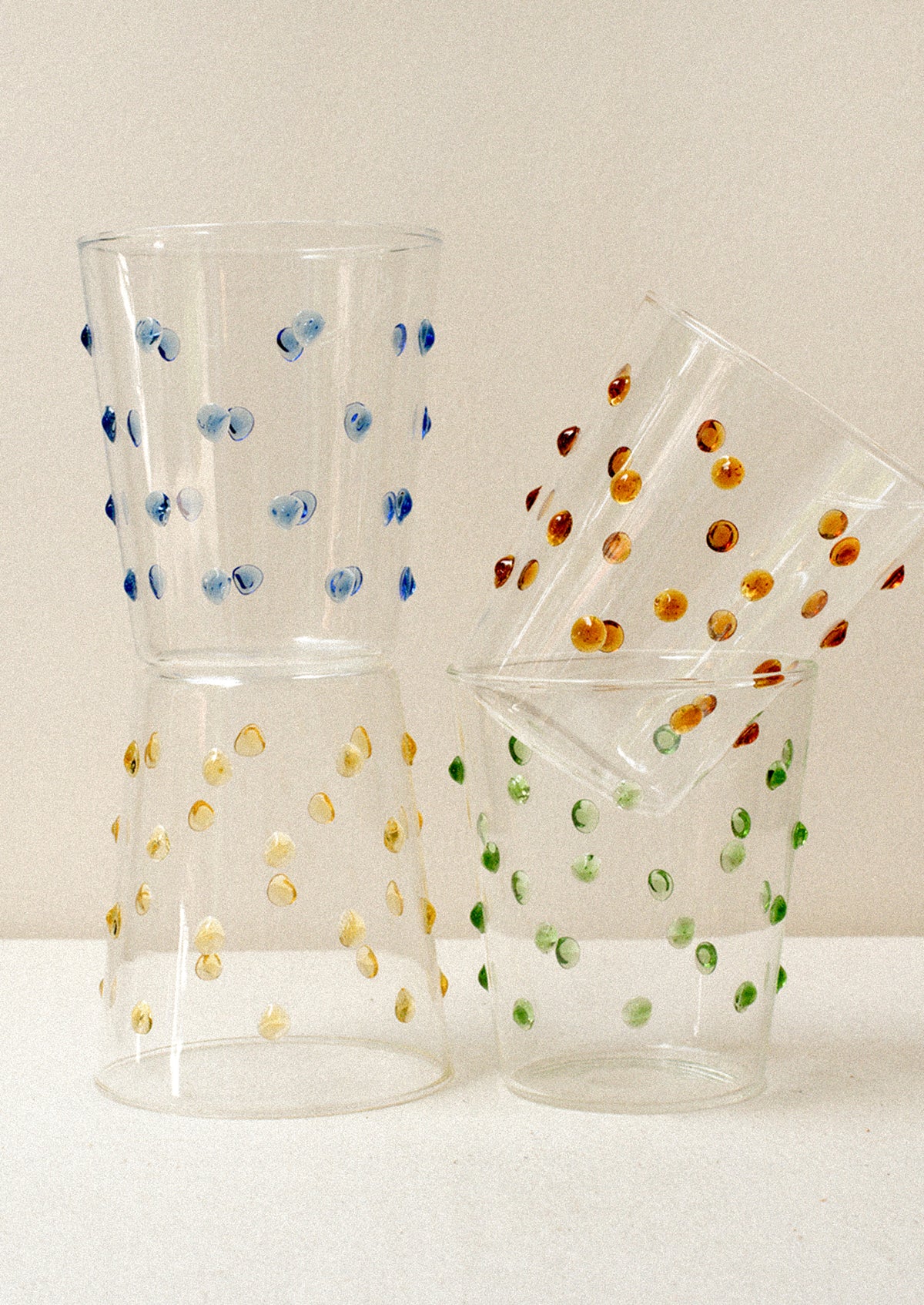 Four clear glass tumblers with textured raised dots on outside, in four color options.