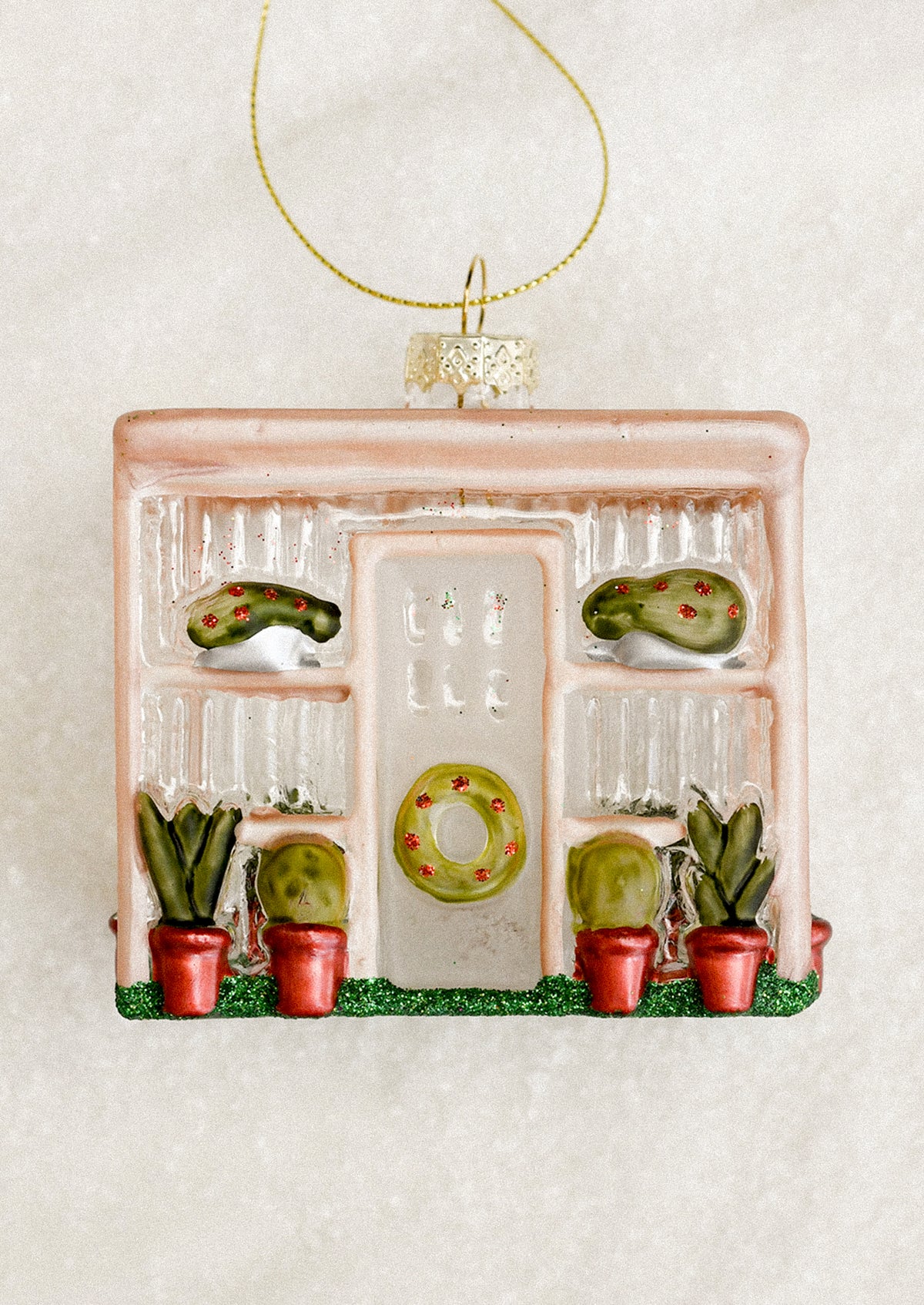 A decorative glass ornament depicting a greenhouse, with wreath decorations.