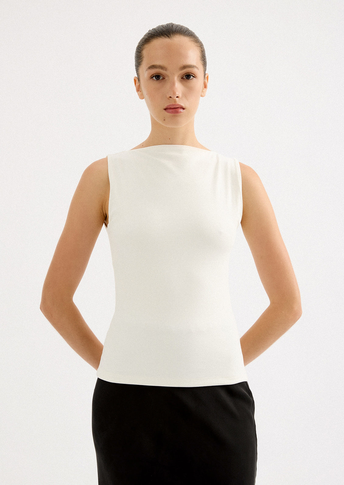 A woman wearing a solid white sleeveless tank top with high round neckline.