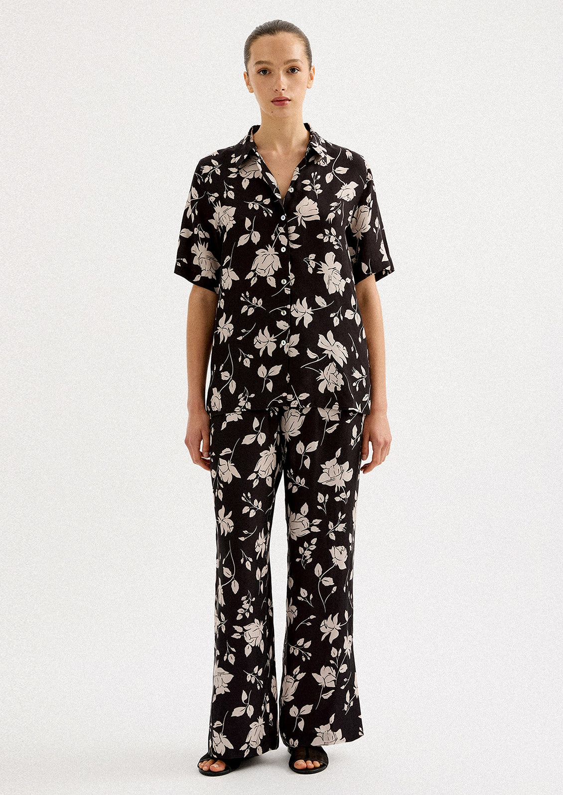 A person wearing a short sleeve collared shirt in black with white floral pattern.