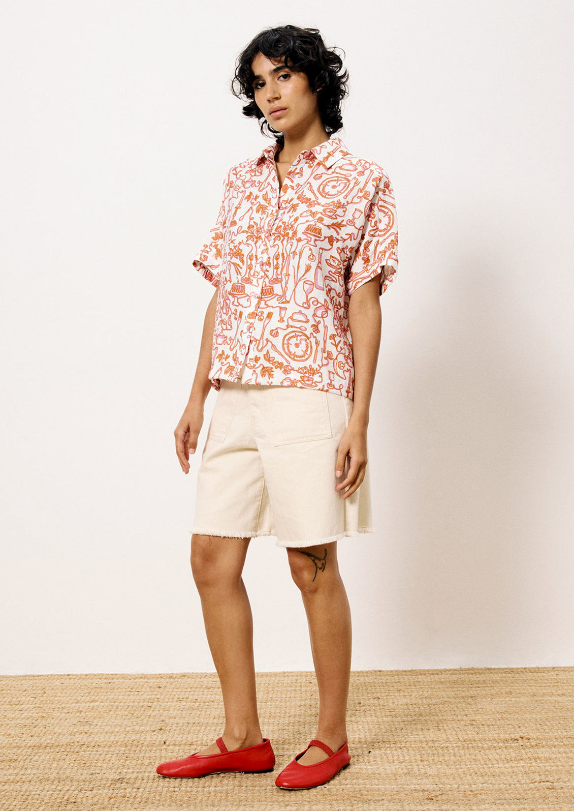 A person wearing a short sleeve button front shirt with pink and orange set the table print.