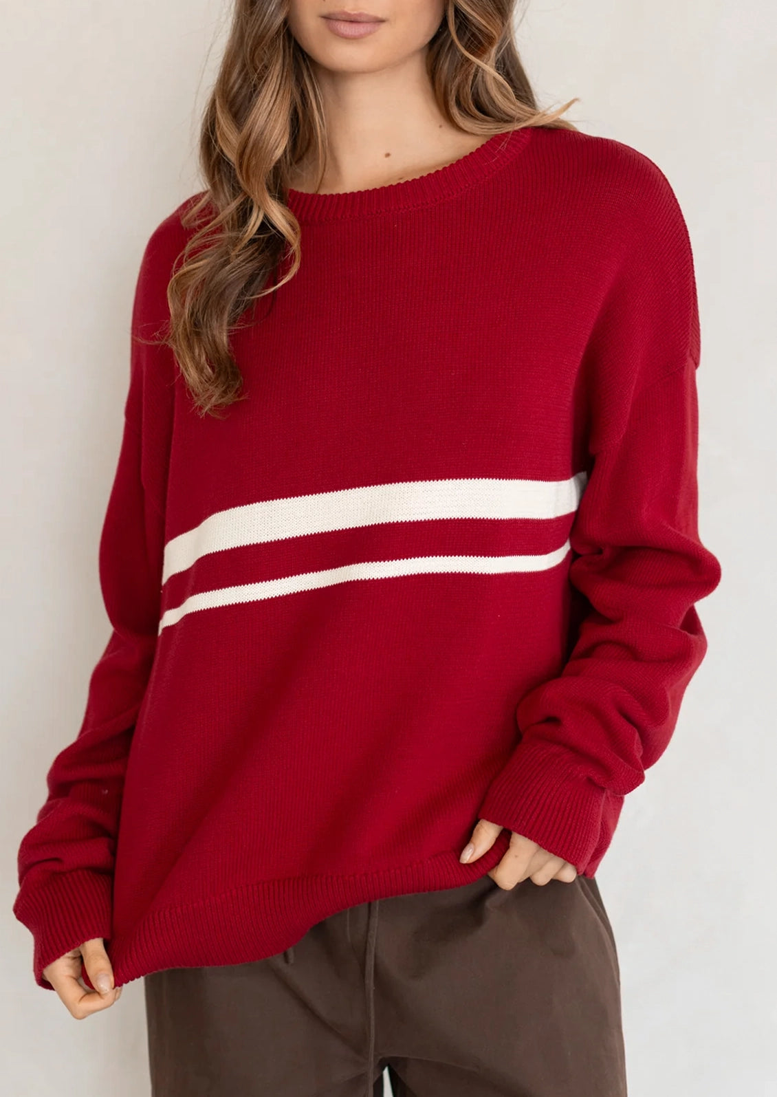 A person wearing a long sleeve cotton sweater in red with two white stripes at middle chest.