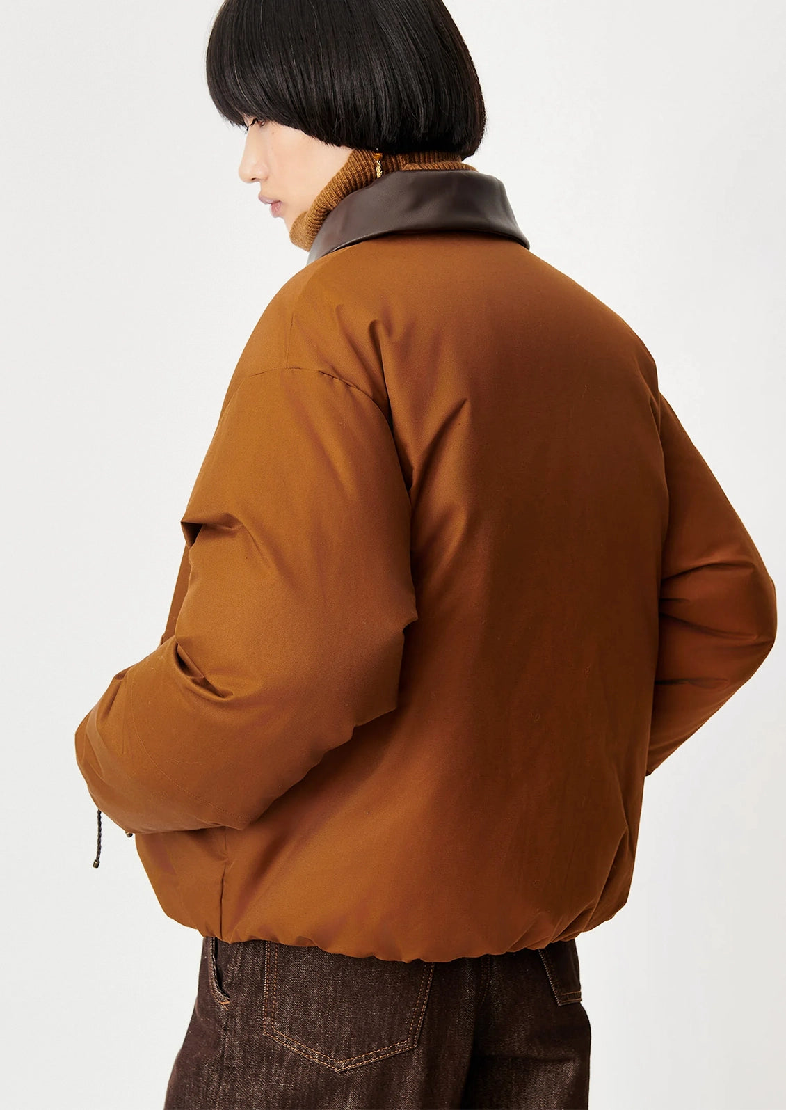 A model shown from the back wearing a brown puffer jacket with a dark brown collar, paired with dark brown pants, against a plain light gray background.