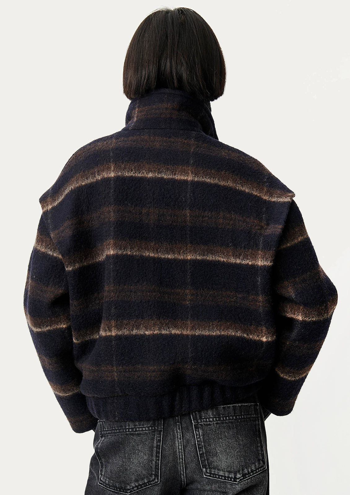 A woman wearing a navy blue and brown plaid short jacket with funnel neck and button front.