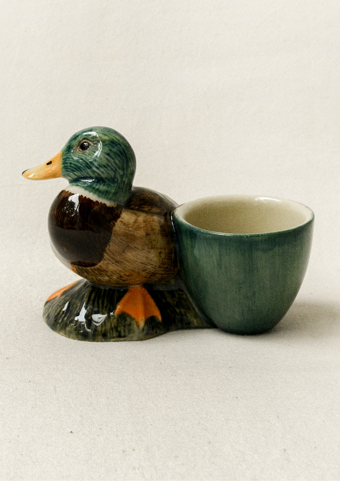 A ceramic duck-shaped cup holder with a small cup attached to its side, shown on a plain light beige background.