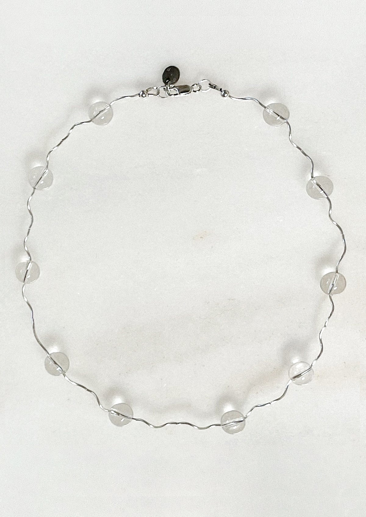 A necklace with a wavy sterling silver band adorned with clear round quartz stations.