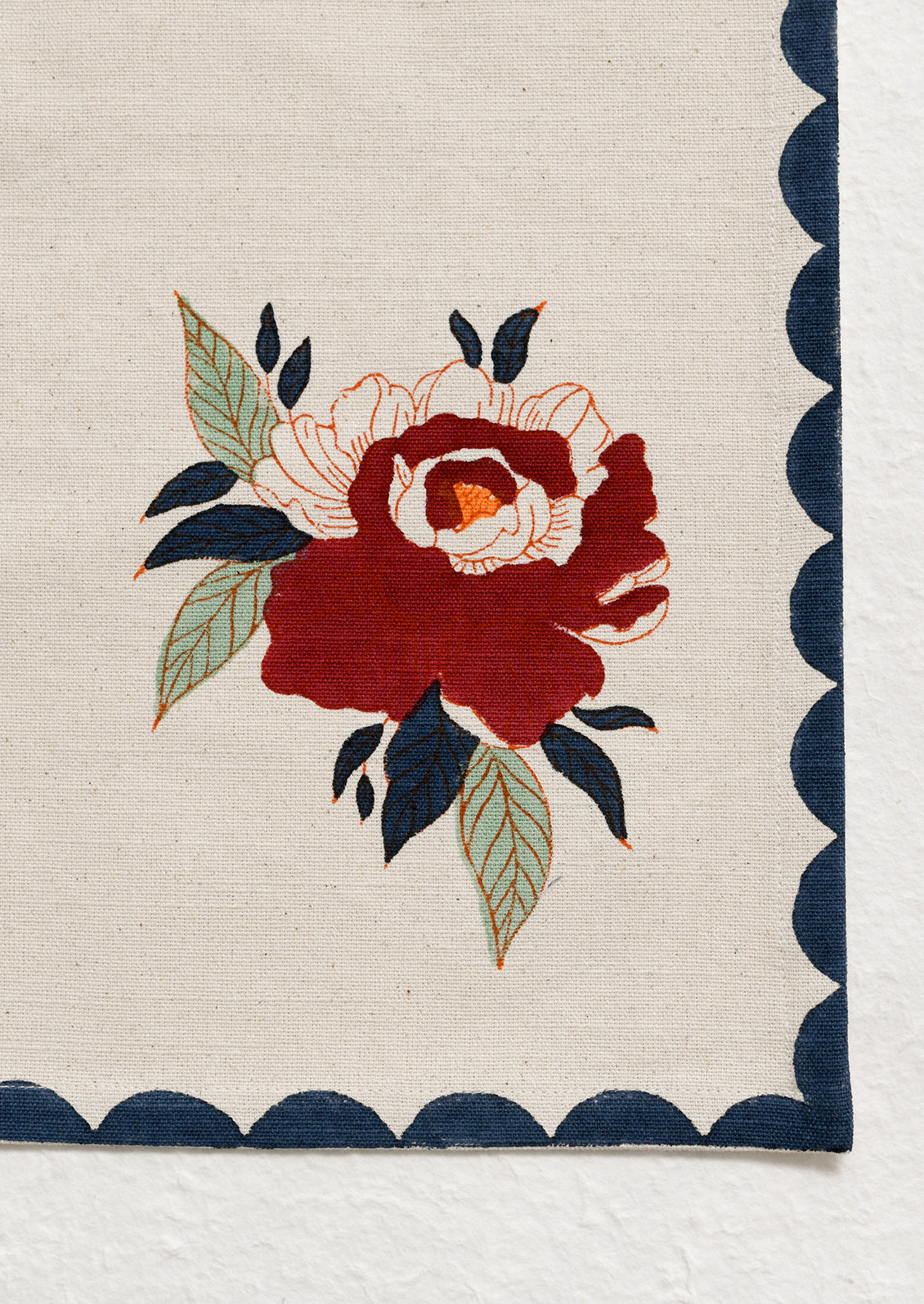 A cotton placemat with two floral peony motifs, with navy scalloped border.