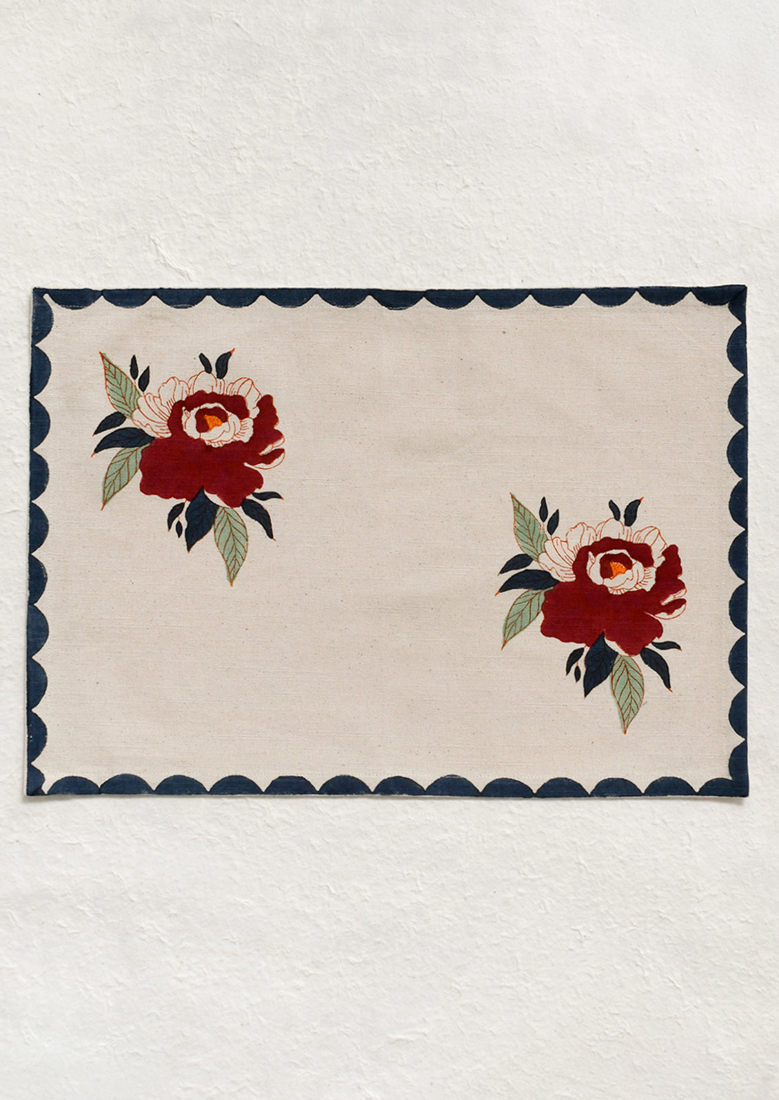 A cotton placemat with two floral peony motifs, with navy scalloped border.