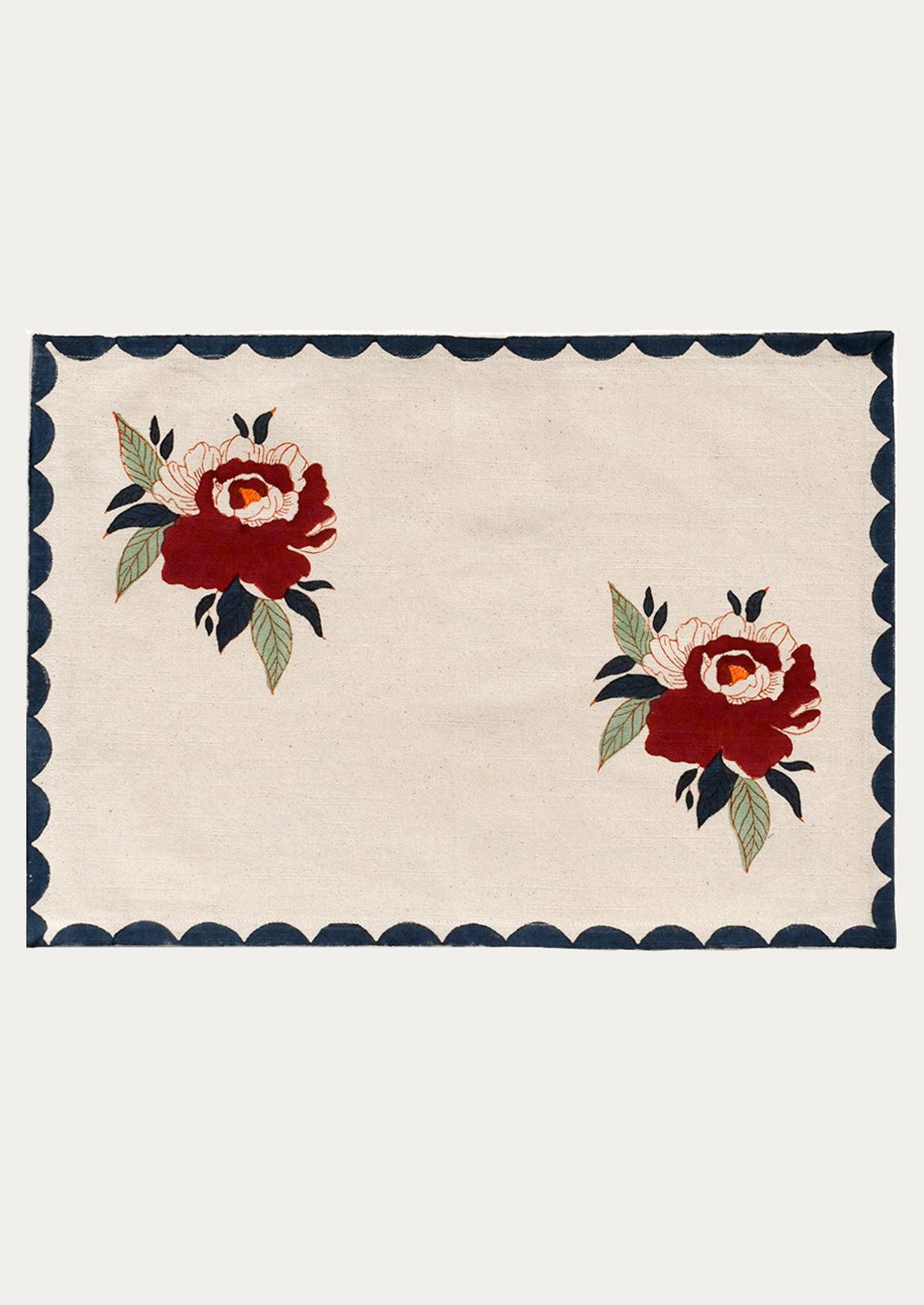 A cotton placemat with two floral peony motifs, with navy scalloped border.