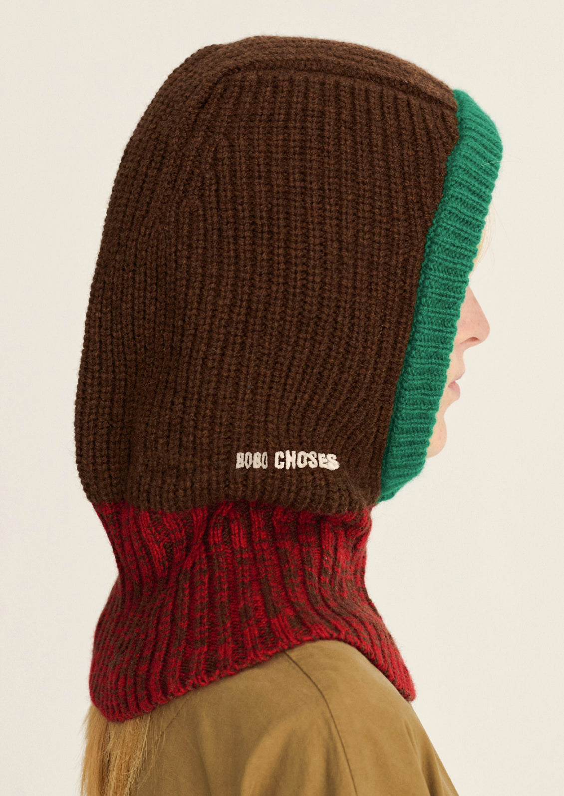 A woman wearing a brown, red, and green color block balaclava with a ribbed knit design.