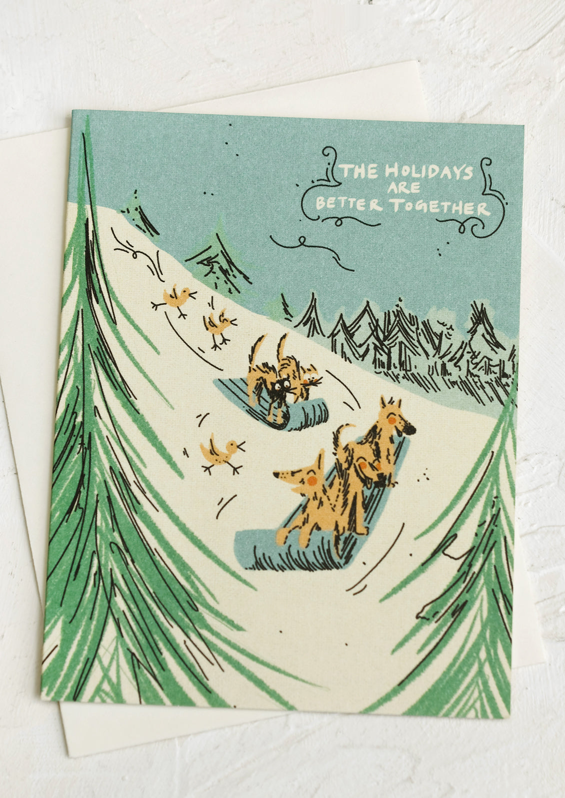 Greeting cards with illustration of dogs sledding down a hill, text reads "The Holidays Are Better Together".