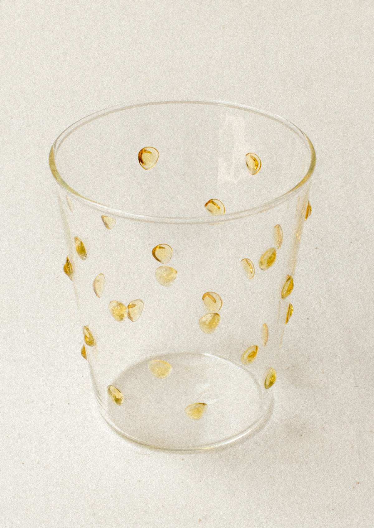A clear glass tumblerswith textured raised dots on outside, in yellow.