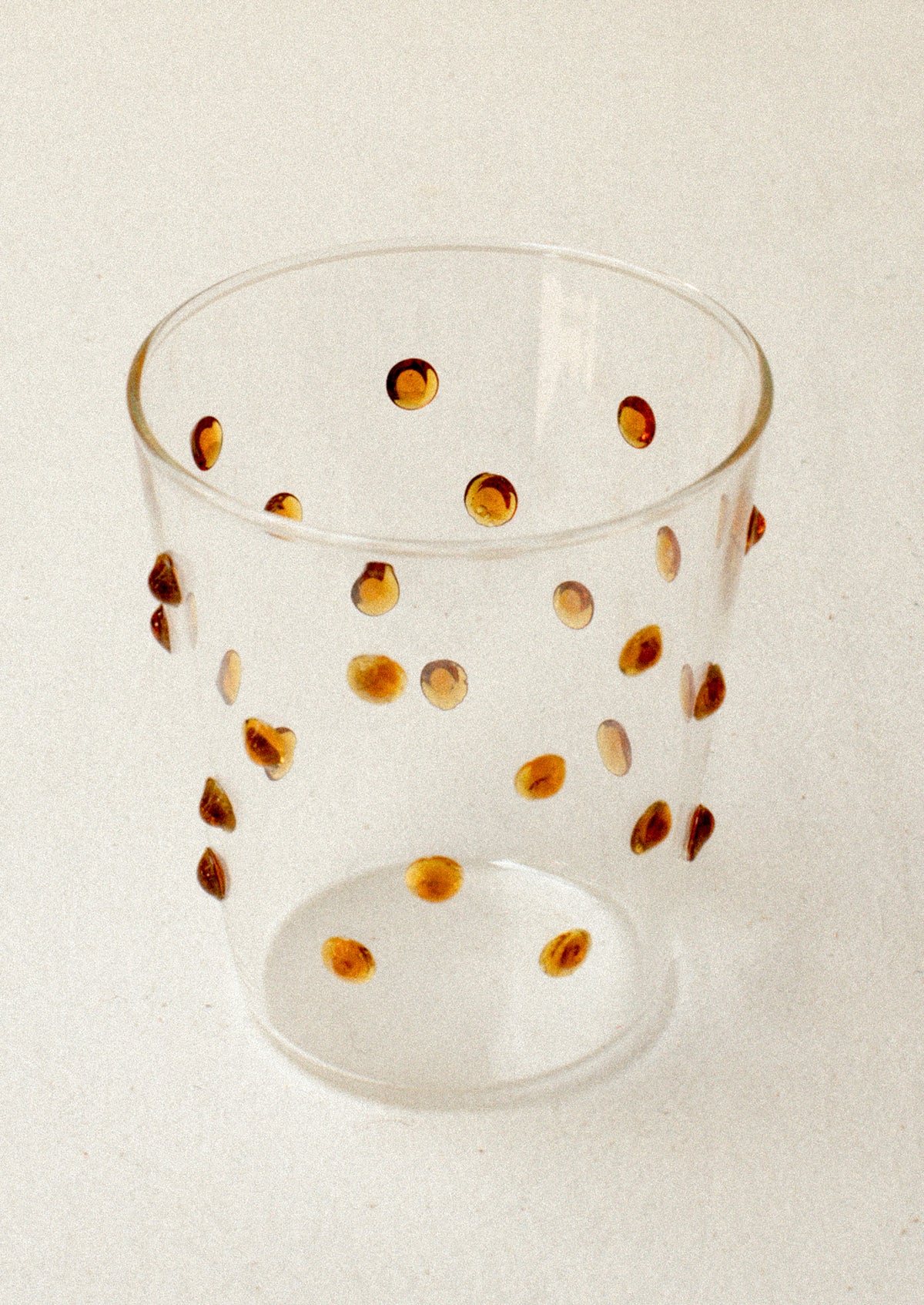 A clear glass tumblerswith textured raised dots on outside, in caramel.