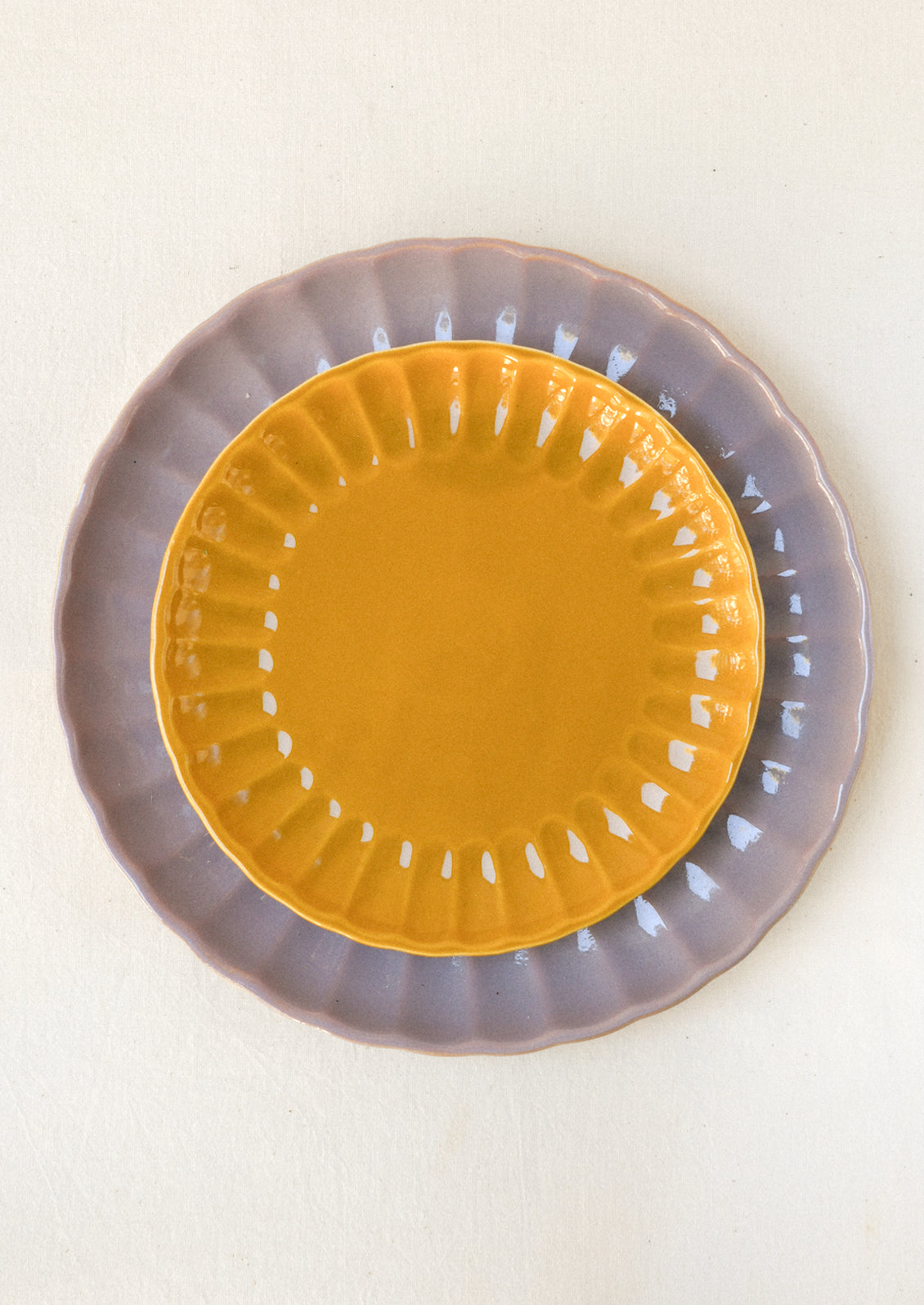 Mustard yellow and lavender ceramic plates stacked together, both with scalloped edges and glossy finishes.