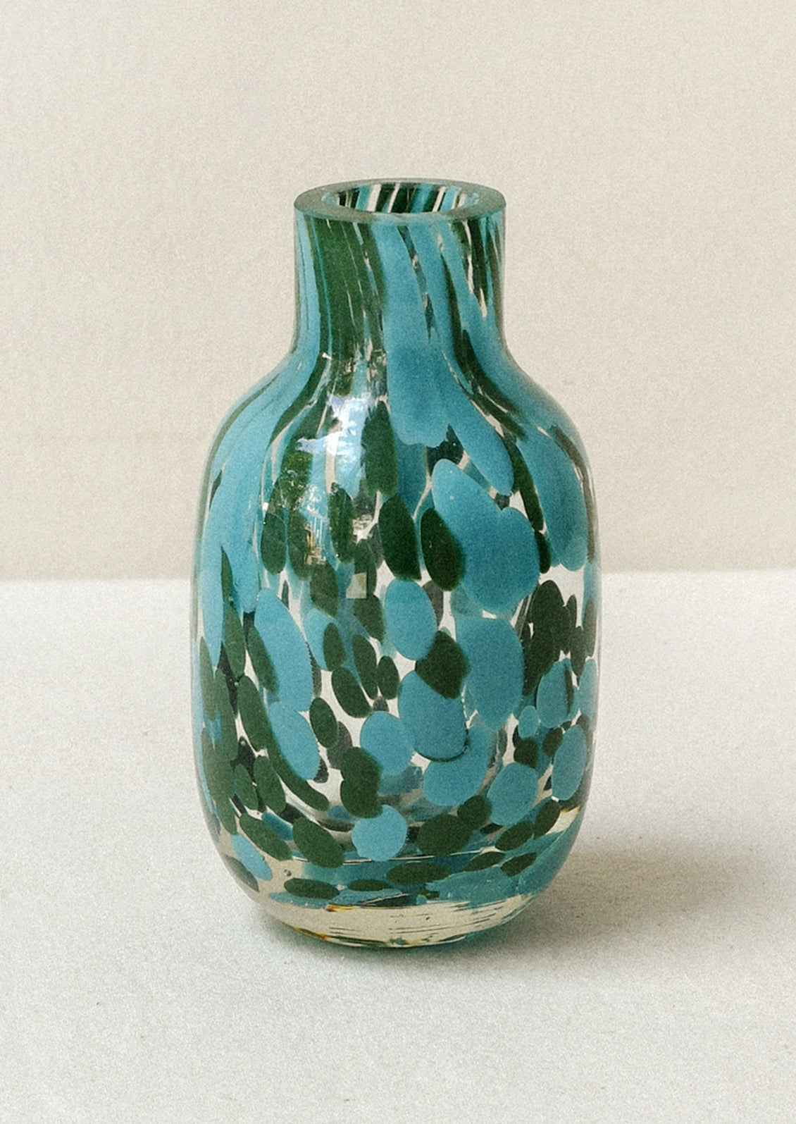 A small glass bud vase with a painted green and teal design.