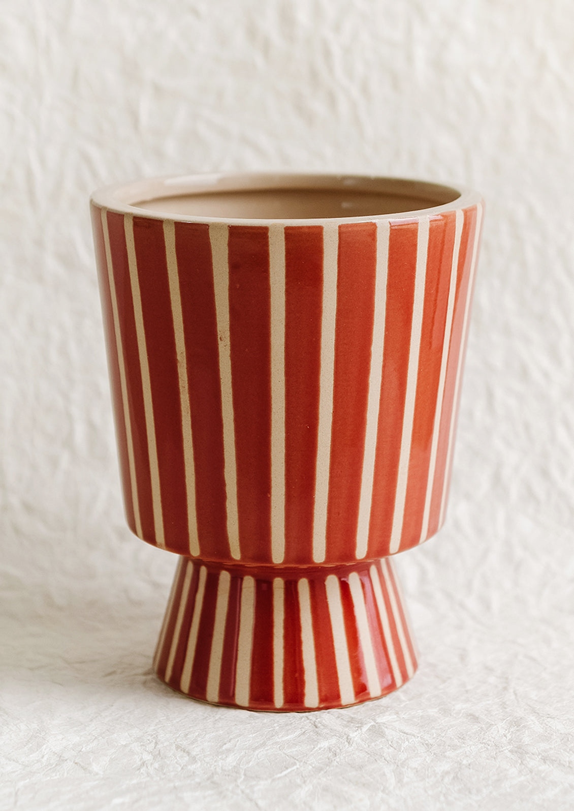 A footed planter with vertical white stripes on red ceramic.