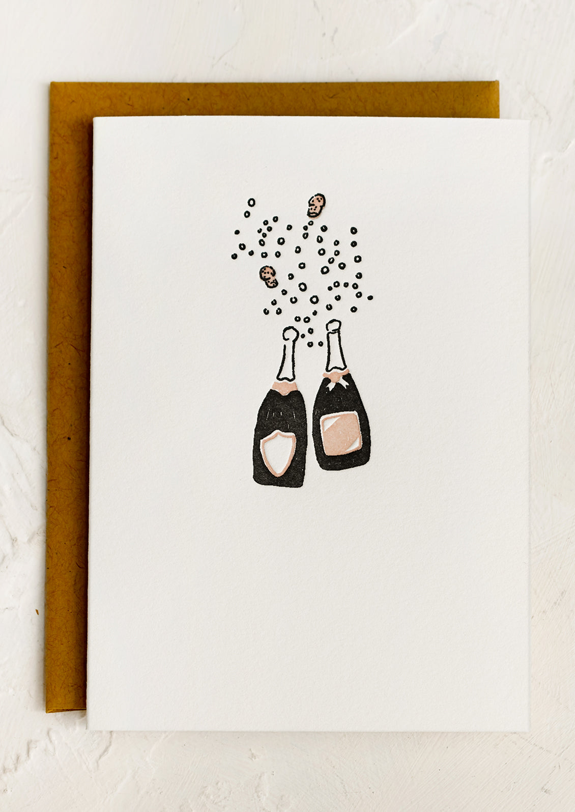 A card with small letterpressd image of two clinking champagne bottles.
