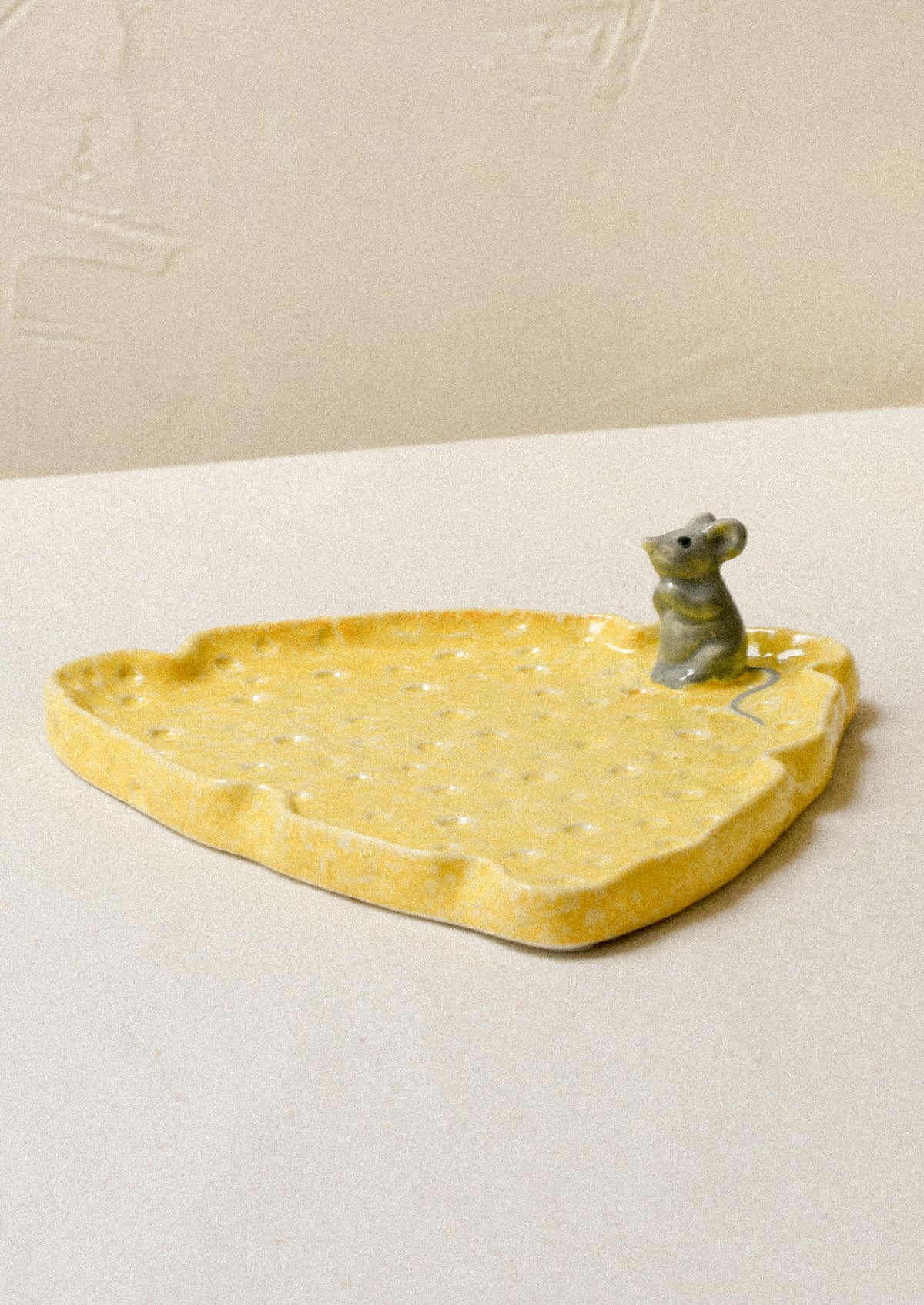 A ceramic plate in the shape of a slice of cheese with a mouse figurine on top.