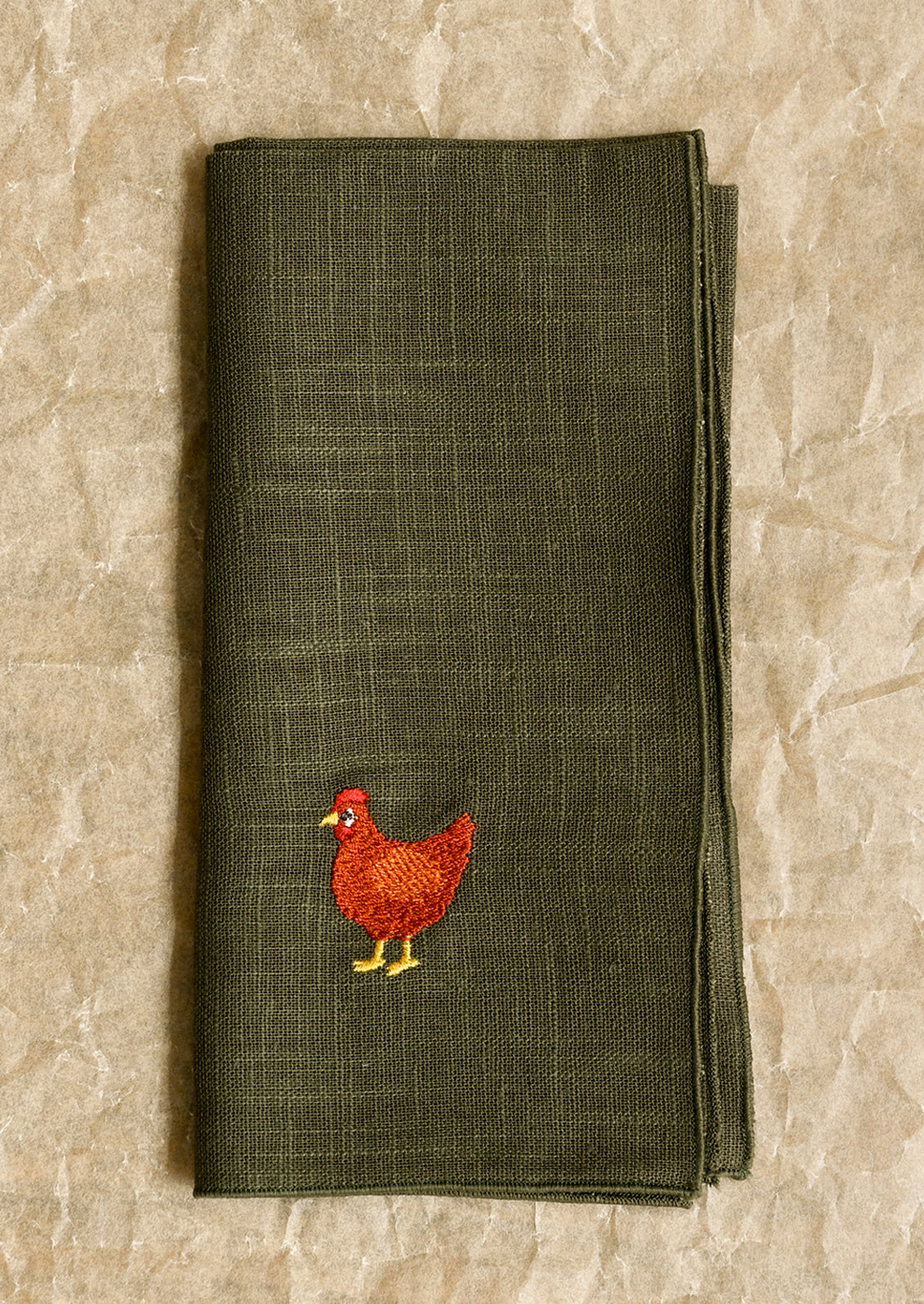 Green napkin with a red chicken embroidery on a beige stone surface