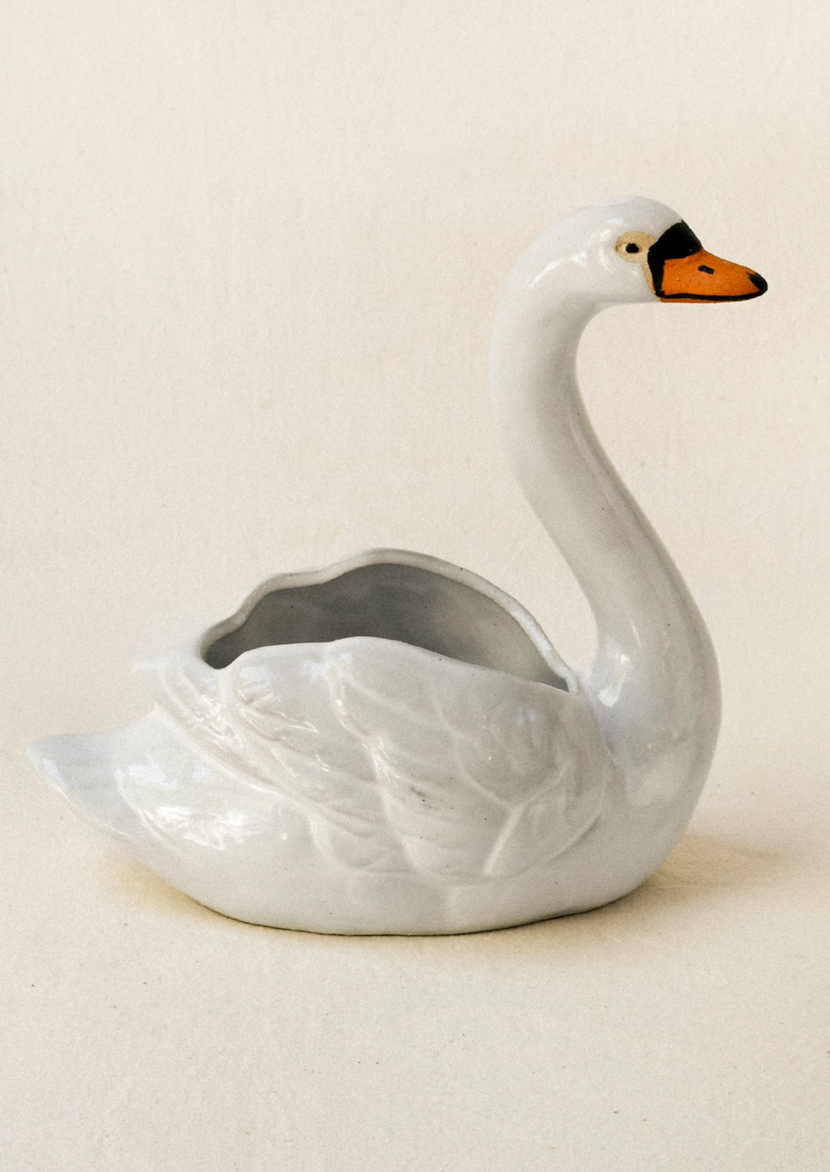 A ceramic planter in the shape of a cygnet sitting atop a table against a beige backdrop.