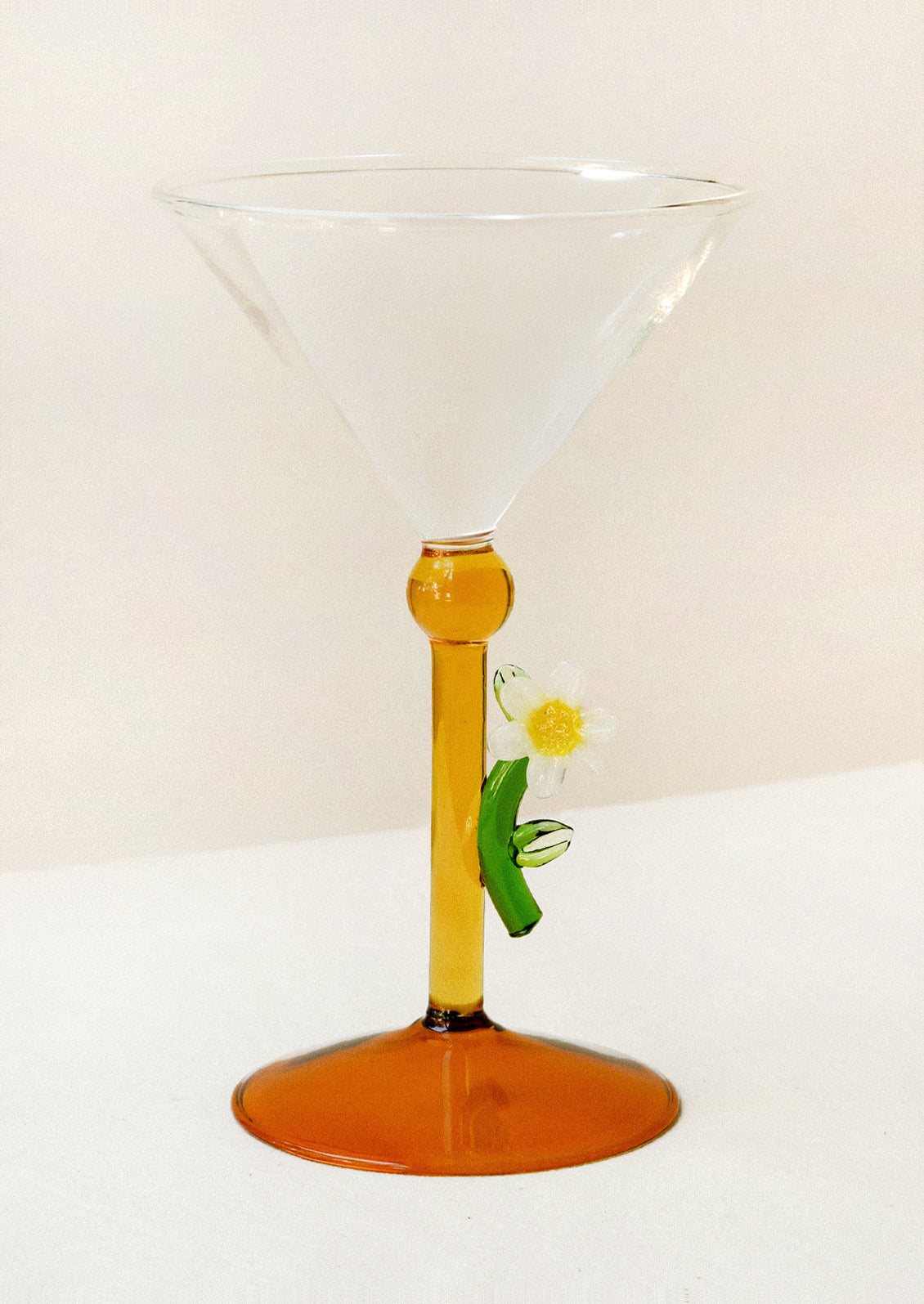 Martini glass with a glass daisy figurine attached to its orange stem.