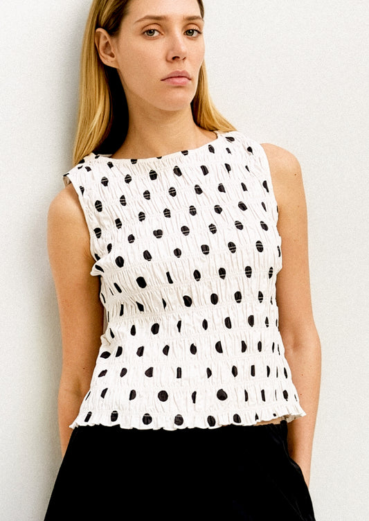 A woman wearing a white sleeveless tank with black polka dots.