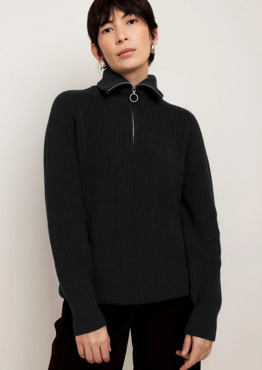 A person wearing a black sweater with silver zip at funnel neck.